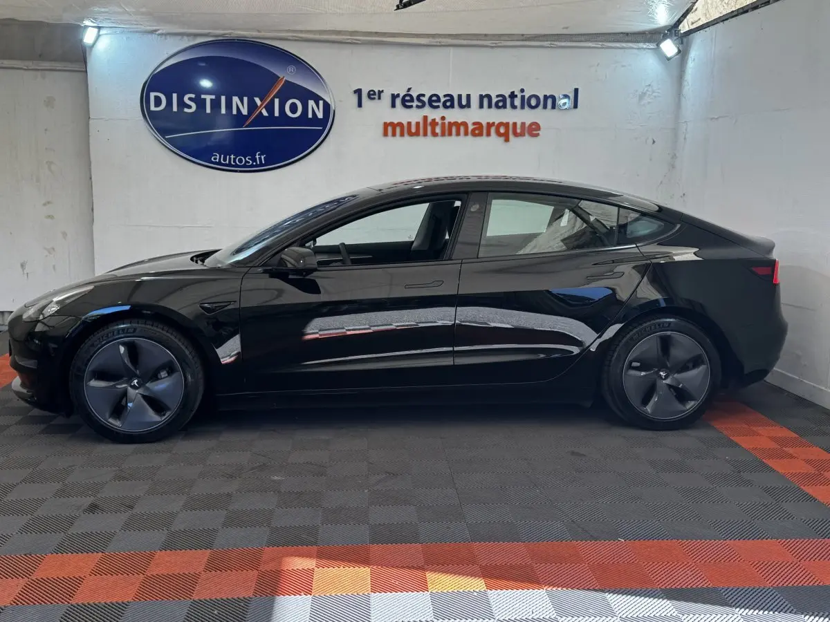 Profil côté gauche d'une Tesla Model 3 noire 2023 Grande Autonomie, roues aérodynamiques et intérieur visible.