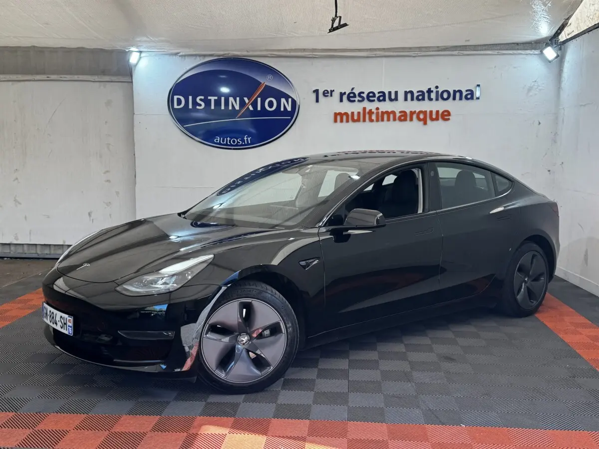 Tesla Model 3 Grande Autonomie noire vue 3/4 avant droit dans un showroom avec sol gris et orange.