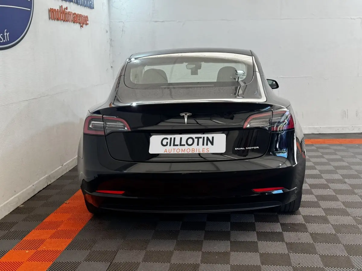 Vue arrière d'une Tesla Model 3 noire 2023 Grande Autonomie, avec feux LED et logo central lumineux.
