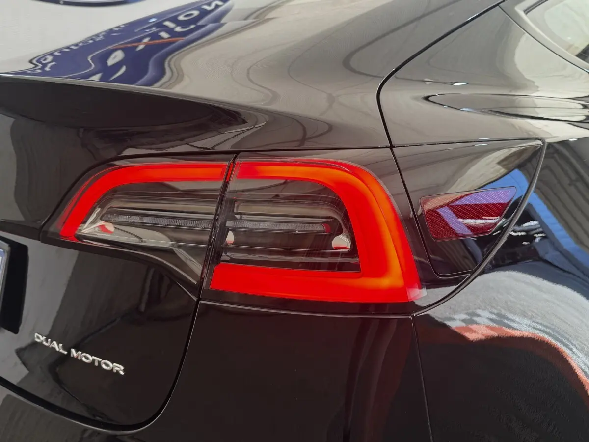 Gros plan sur le feu arrière droit rouge vif d’une Tesla Model 3 Grande Autonomie noire 2023, avec logo Dual Motor.