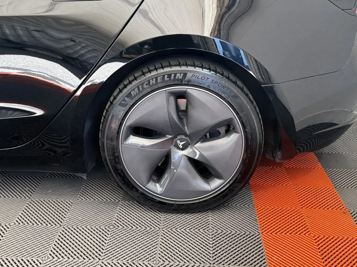 Gros plan sur la roue arrière droite noire d'une Tesla Model 3 2023 avec jante aérodynamique et pneu Michelin Pilot Sport.