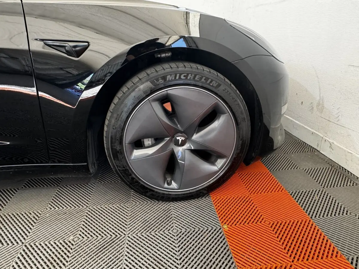 Gros plan sur la roue avant gauche noire d'une Tesla Model 3 2023 avec jante aérodynamique et logo Tesla central.