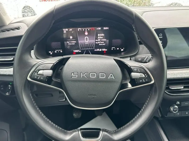 Vue rapprochée du volant cuir noir multifonction SKODA avec tableau de bord numérique allumé sur fond gris.