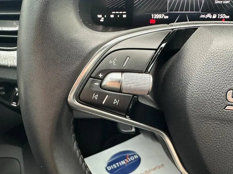 Gros plan sur les commandes audio au volant cuir noir de la Skoda Scala blanc cristal, avec écran digital en arrière-plan.