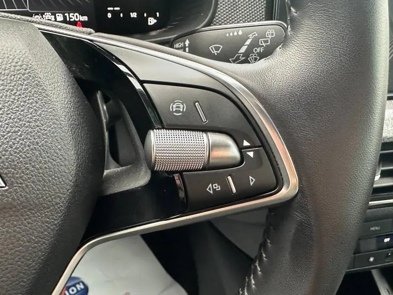 Gros plan sur les commandes multifonctions en métal brossé du volant cuir noir d'une Skoda Scala blanc cristal.