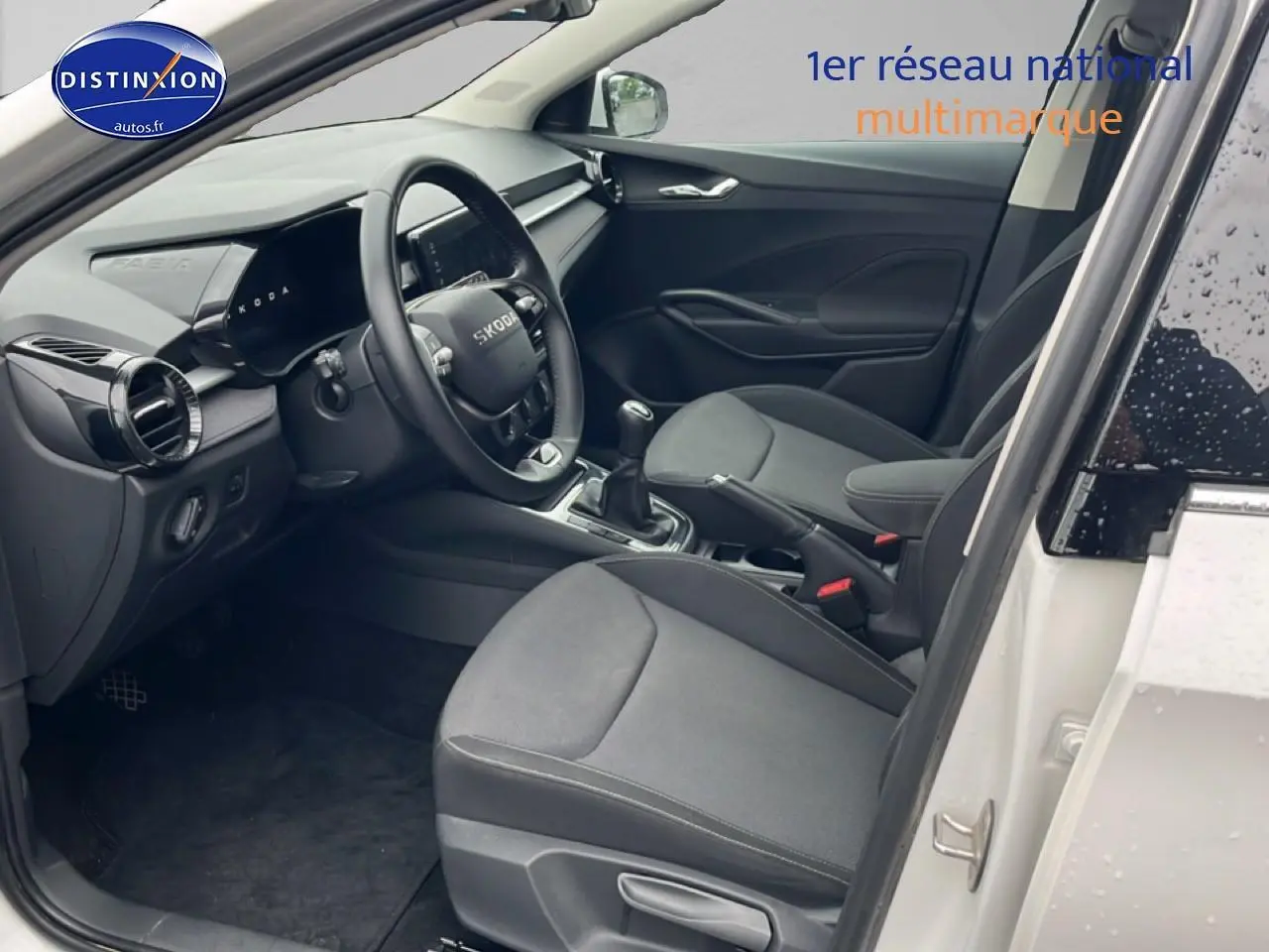 Intérieur avant droit d’une Skoda Fabia blanche 2025, volant cuir multifonction et sièges tissu gris.