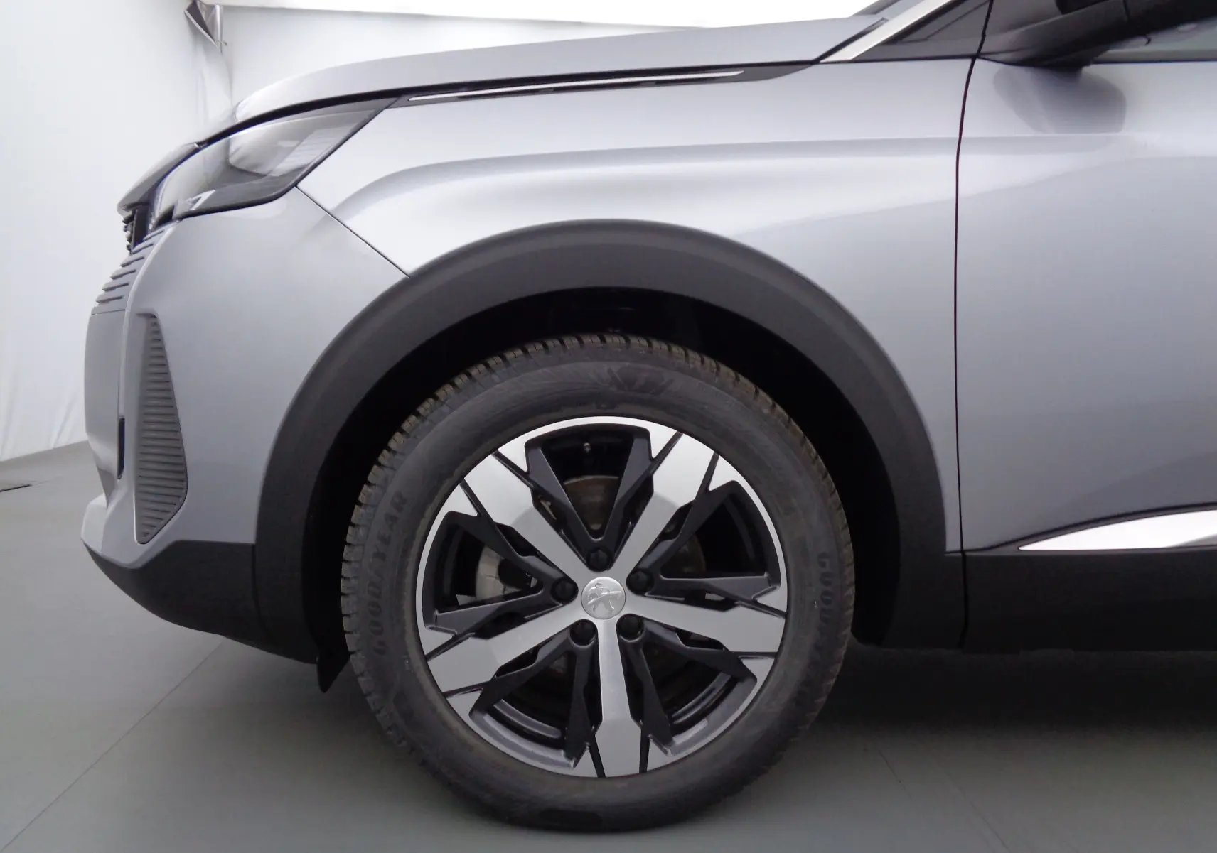 Gros plan sur la roue avant gauche et l'aile d'un Peugeot 3008 gris Artense métal avec jante bi-ton moderne.