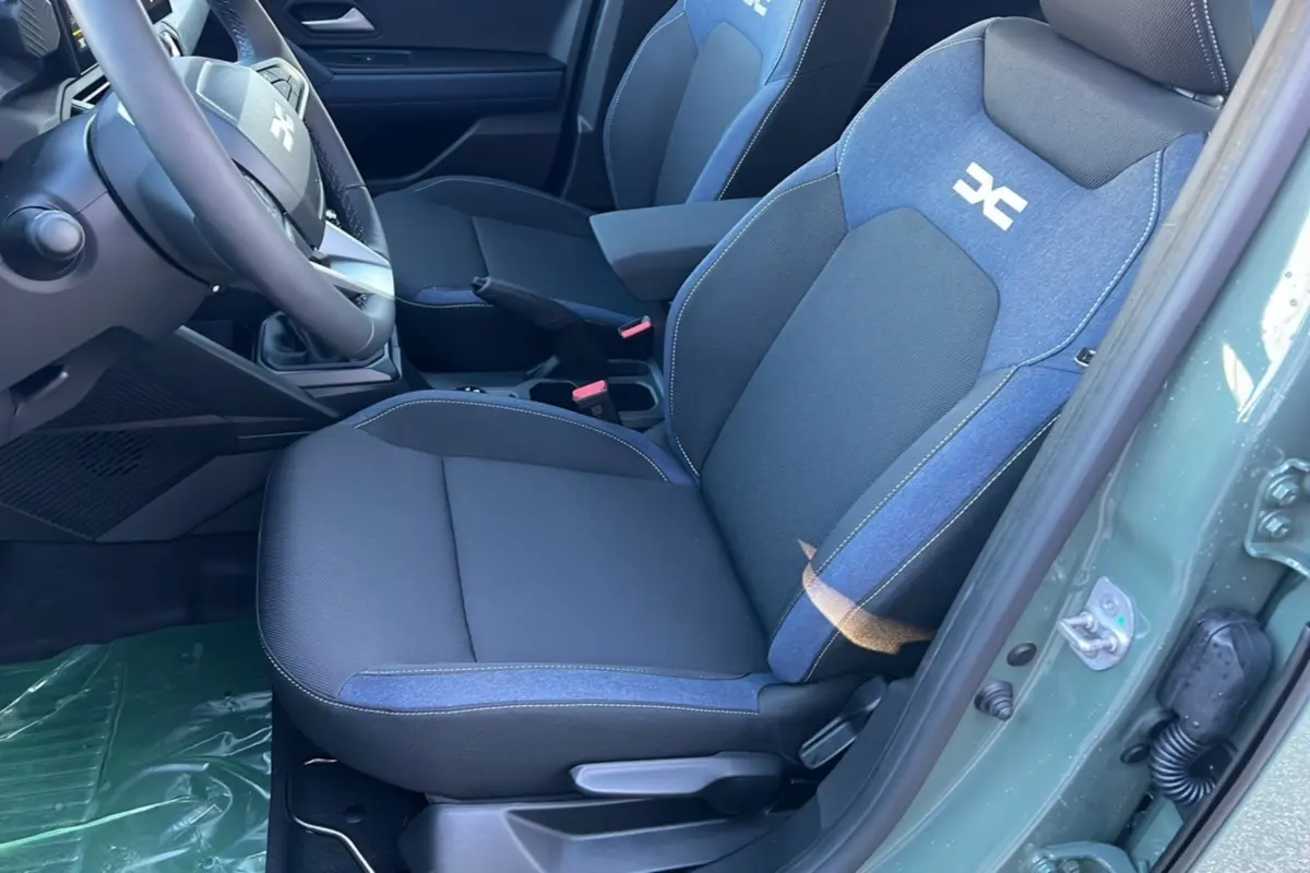 Intérieur du Dacia Duster 2025, siège avant droit en tissu noir et bleu avec logo blanc, portière kaki lichen ouverte.