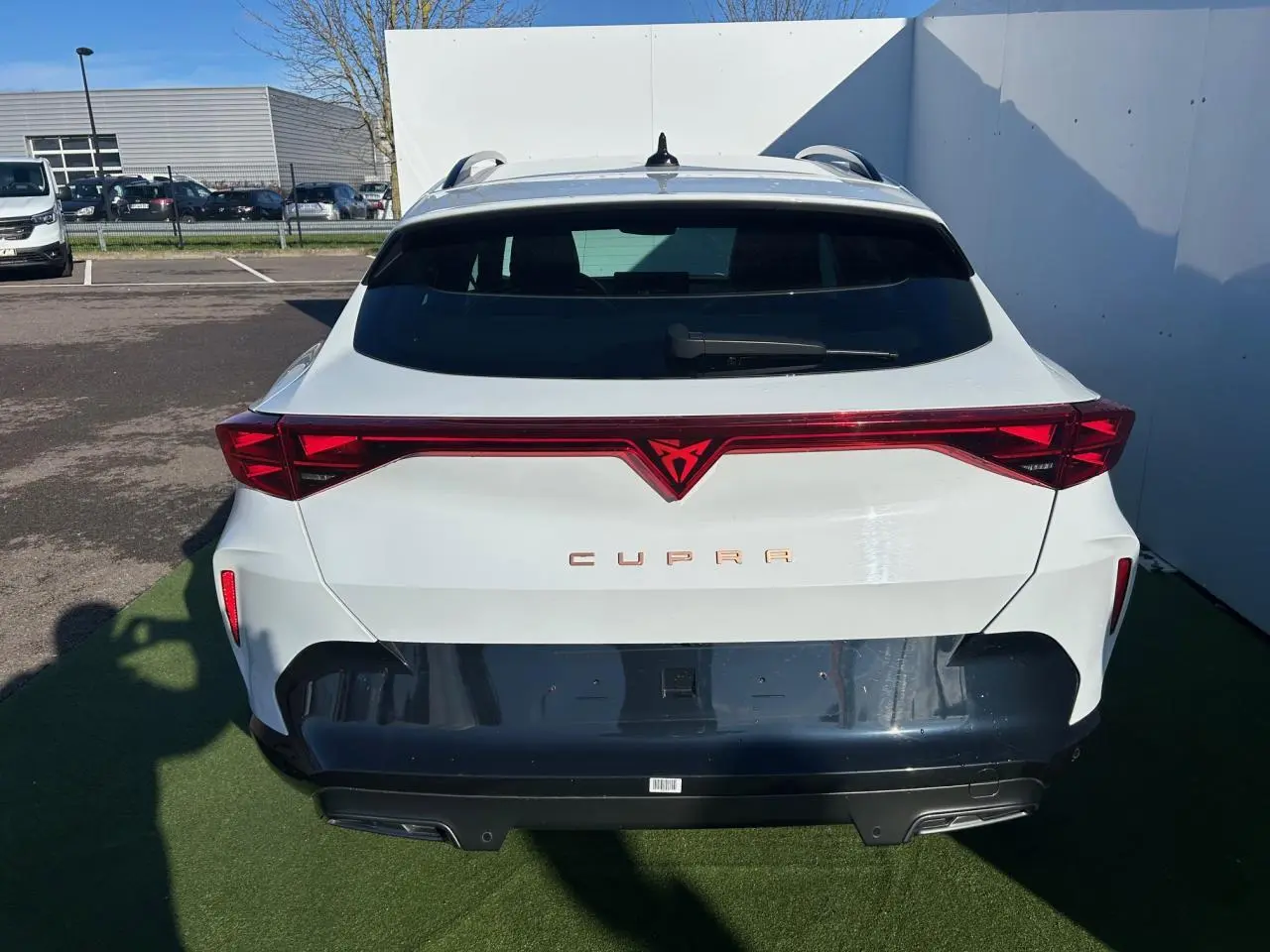 Vue arrière d'un CUPRA Formentor blanc neige avec bandeau lumineux rouge et diffuseur noir contrastant.