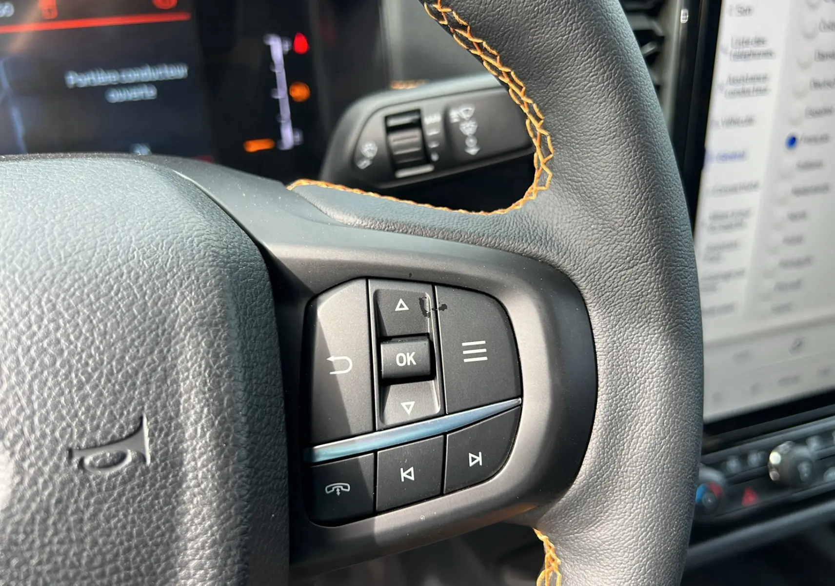 Gros plan sur le volant cuir noir avec surpiqûres orange du Ford Ranger Wildtrak 2026, boutons multifonctions visibles.