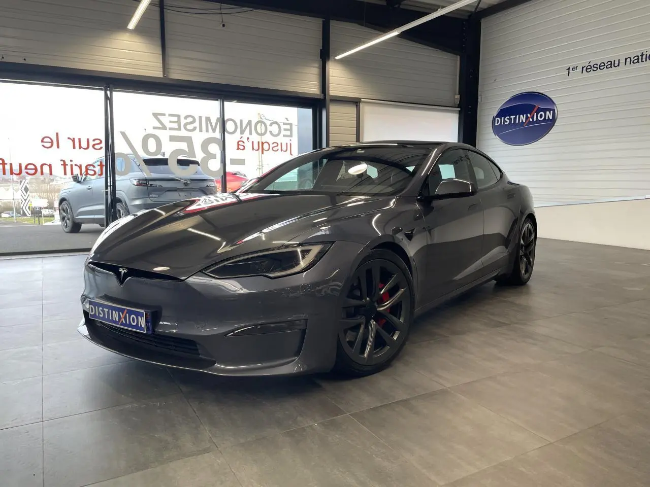 Tesla Model S Plaid gris foncé vue 3/4 avant droit en intérieur avec jantes noires et étriers rouges visibles.