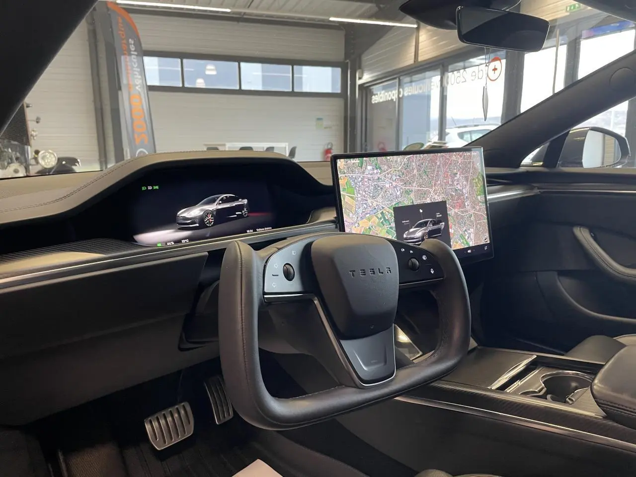 Vue intérieure côté conducteur du Tesla Model S Plaid 2023 avec volant carré et écran tactile central affichant une carte.