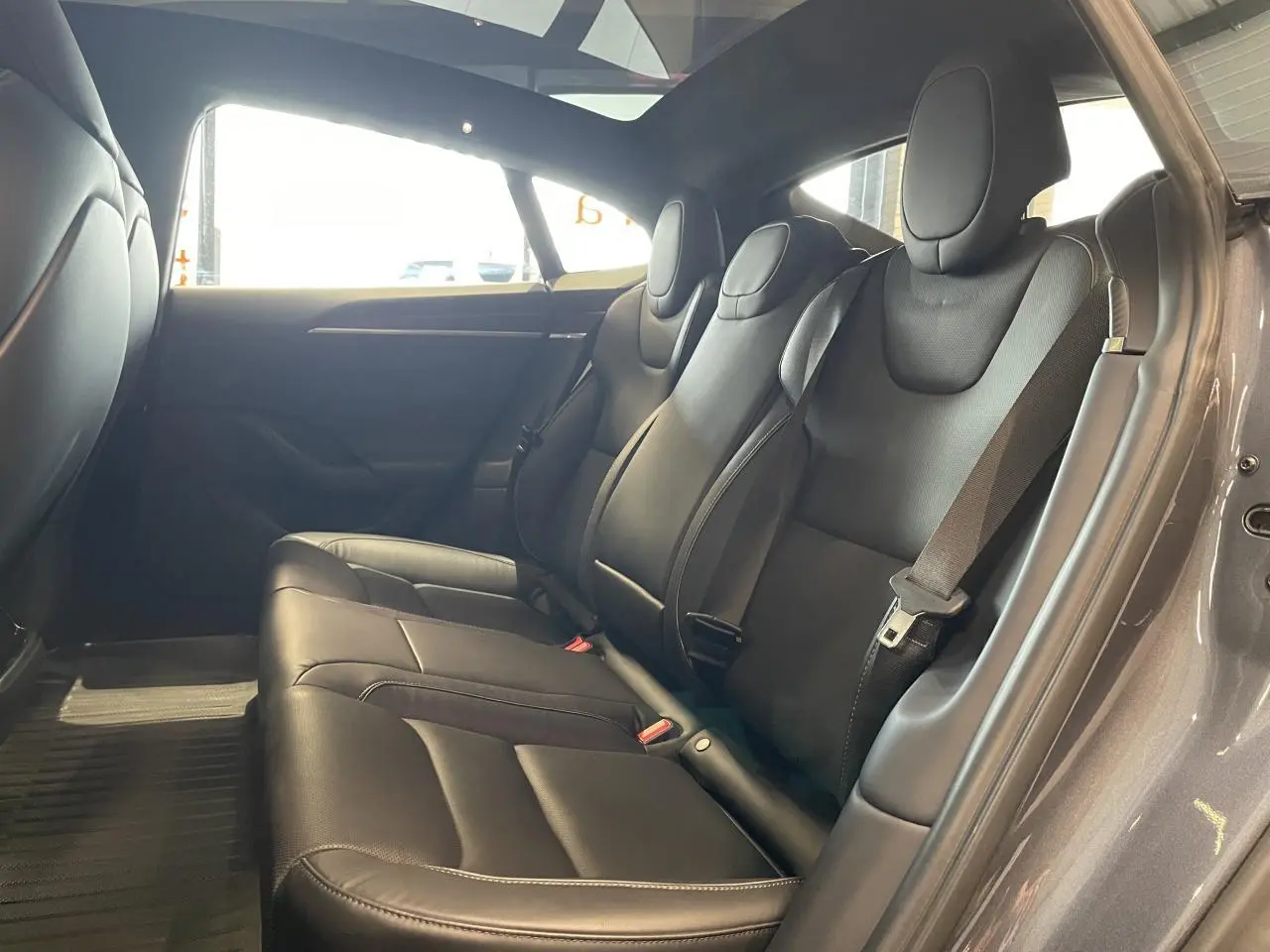 Vue intérieure côté droit des sièges arrière noirs en cuir d'une Tesla Model S Plaid 2023 gris foncé avec ceintures de sécurité visibles.