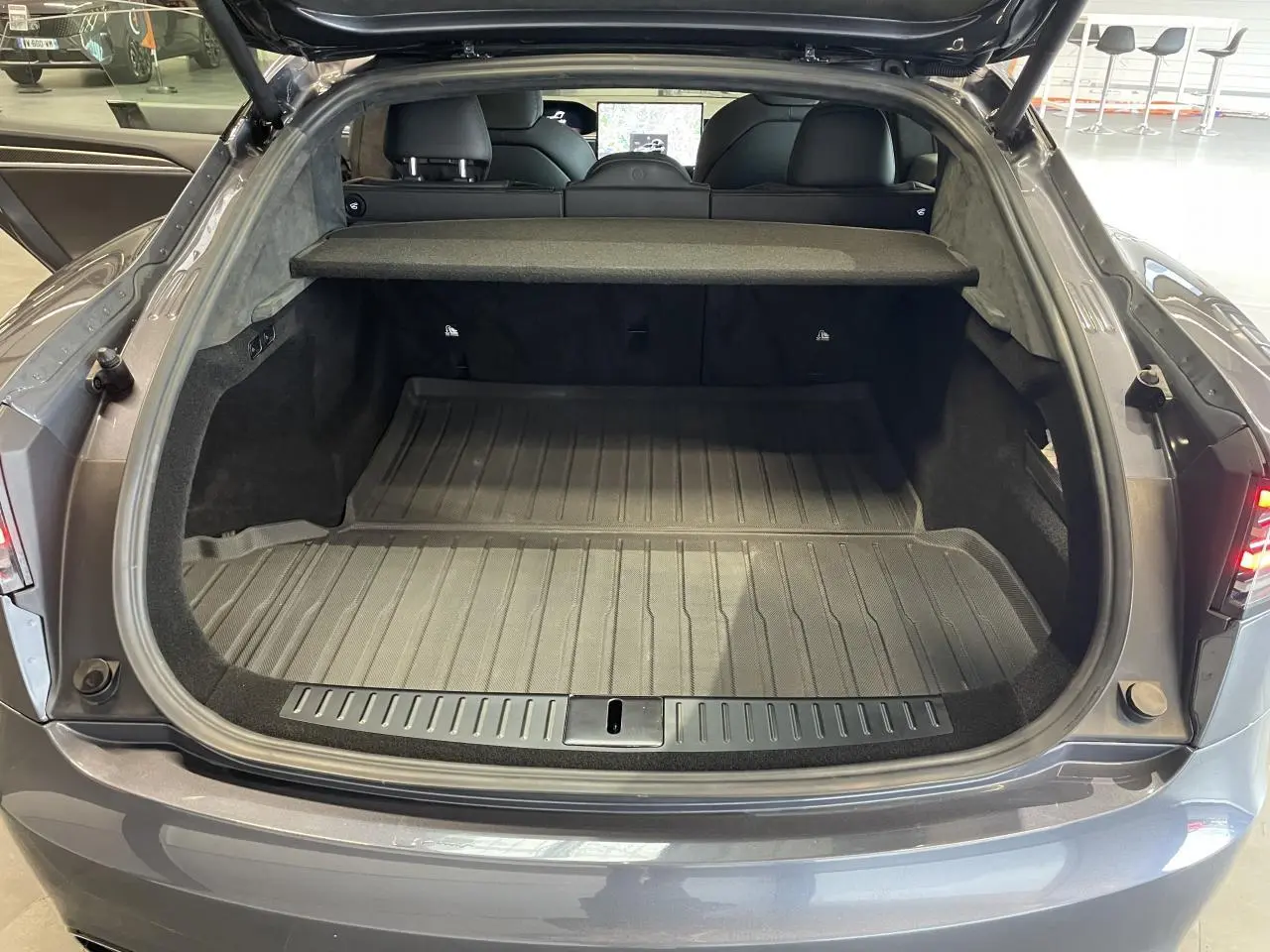 Coffre ouvert vu de l'arrière d'une Tesla Model S Plaid gris foncé avec cache-bagages et intérieur noir.