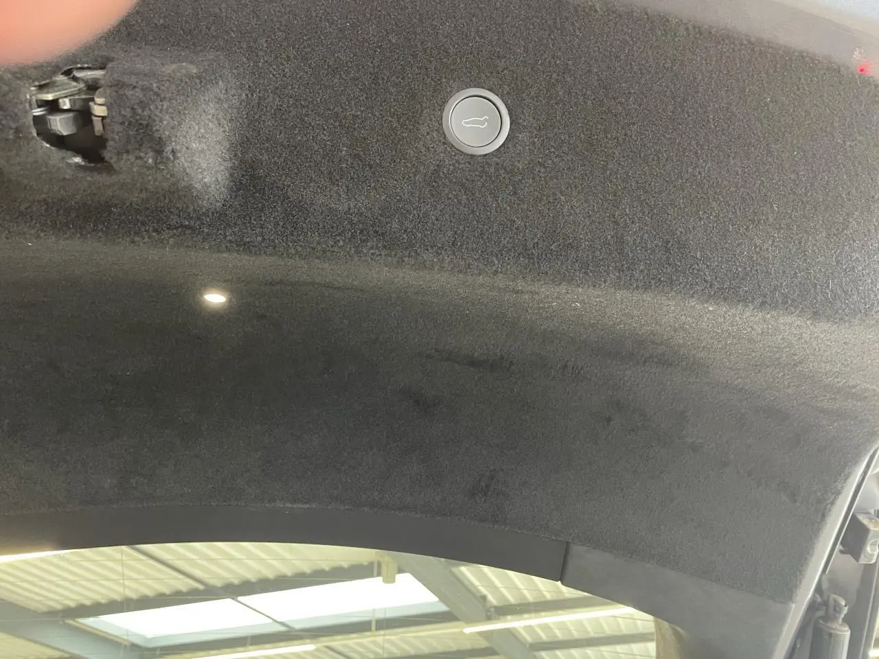 Détail intérieur du coffre ouvert d'une Tesla Model S Plaid gris foncé, montrant la garniture et le bouton de fermeture.