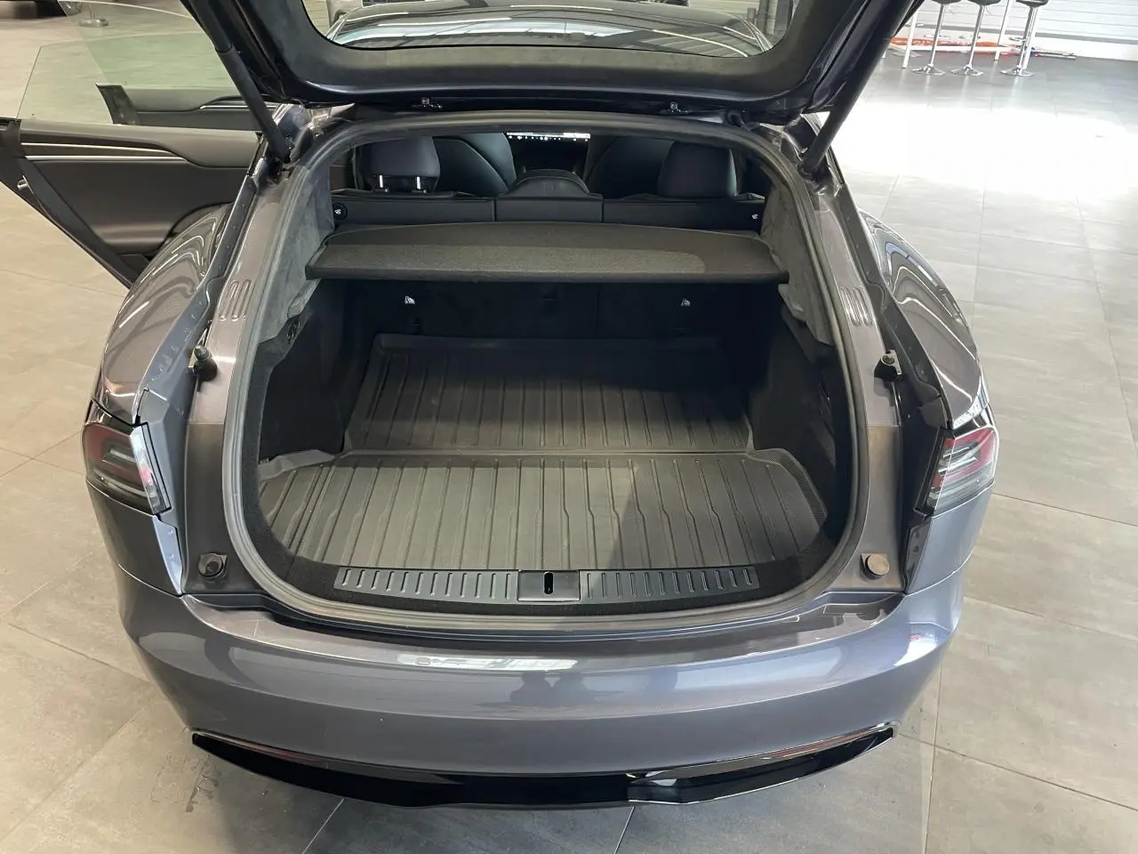 Vue arrière ouverte du coffre d'une Tesla Model S Plaid gris foncé, montrant l'espace de chargement et l'intérieur noir.
