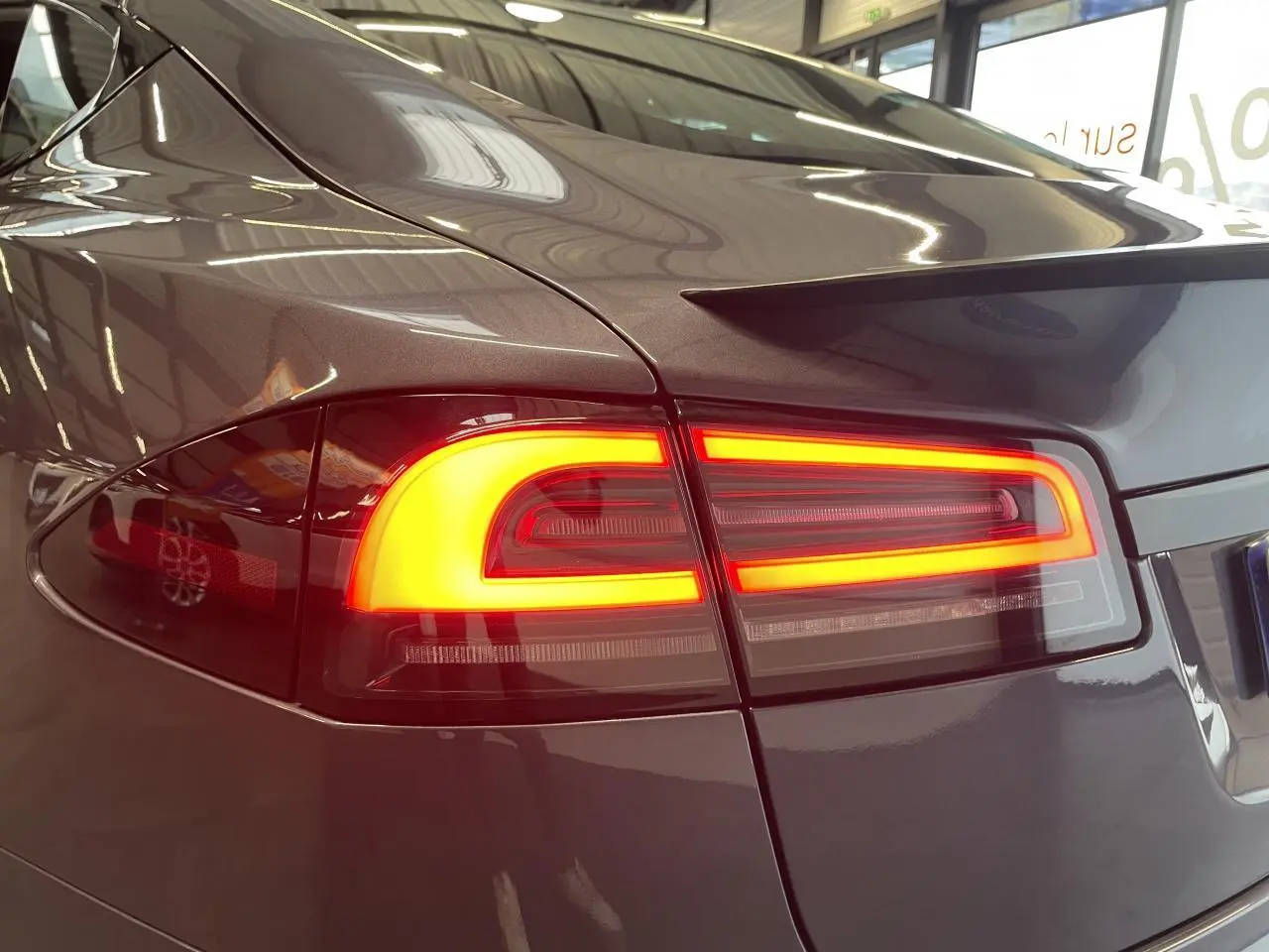 Gros plan sur le feu arrière droit allumé d’une Tesla Model S Plaid gris foncé, soulignant la finition métallique.