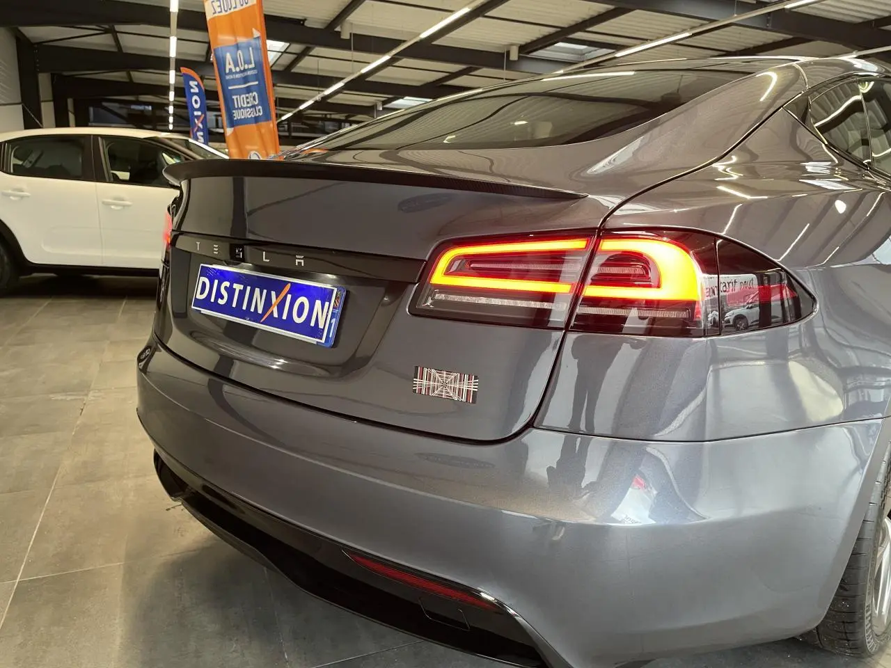 Vue 3/4 arrière droite d'une Tesla Model S Plaid gris foncé avec feux arrière LED allumés en showroom.