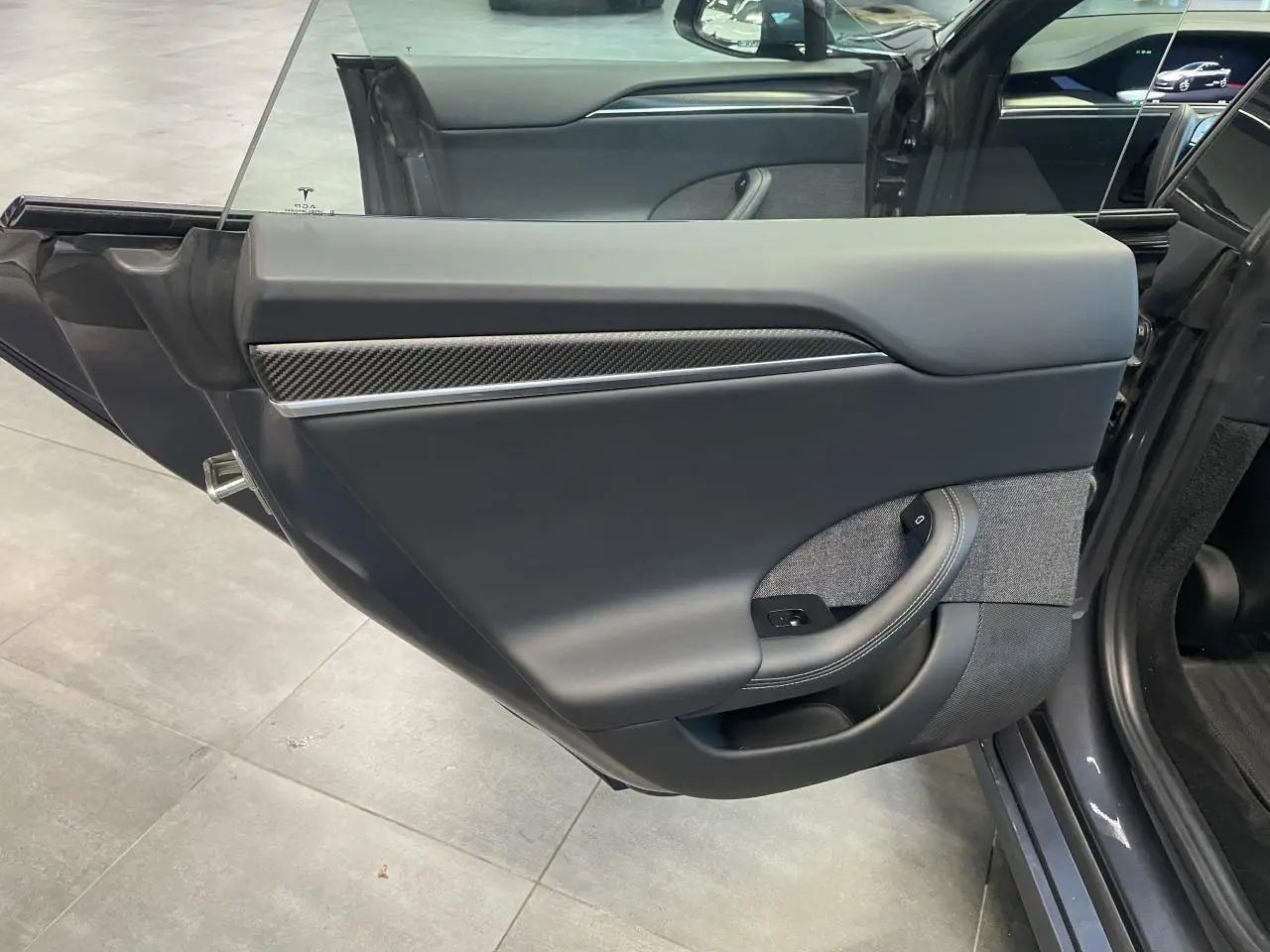 Vue intérieure de la porte arrière gauche gris foncé d'une Tesla Model S Plaid 2023 avec insert carbone et tissu gris.