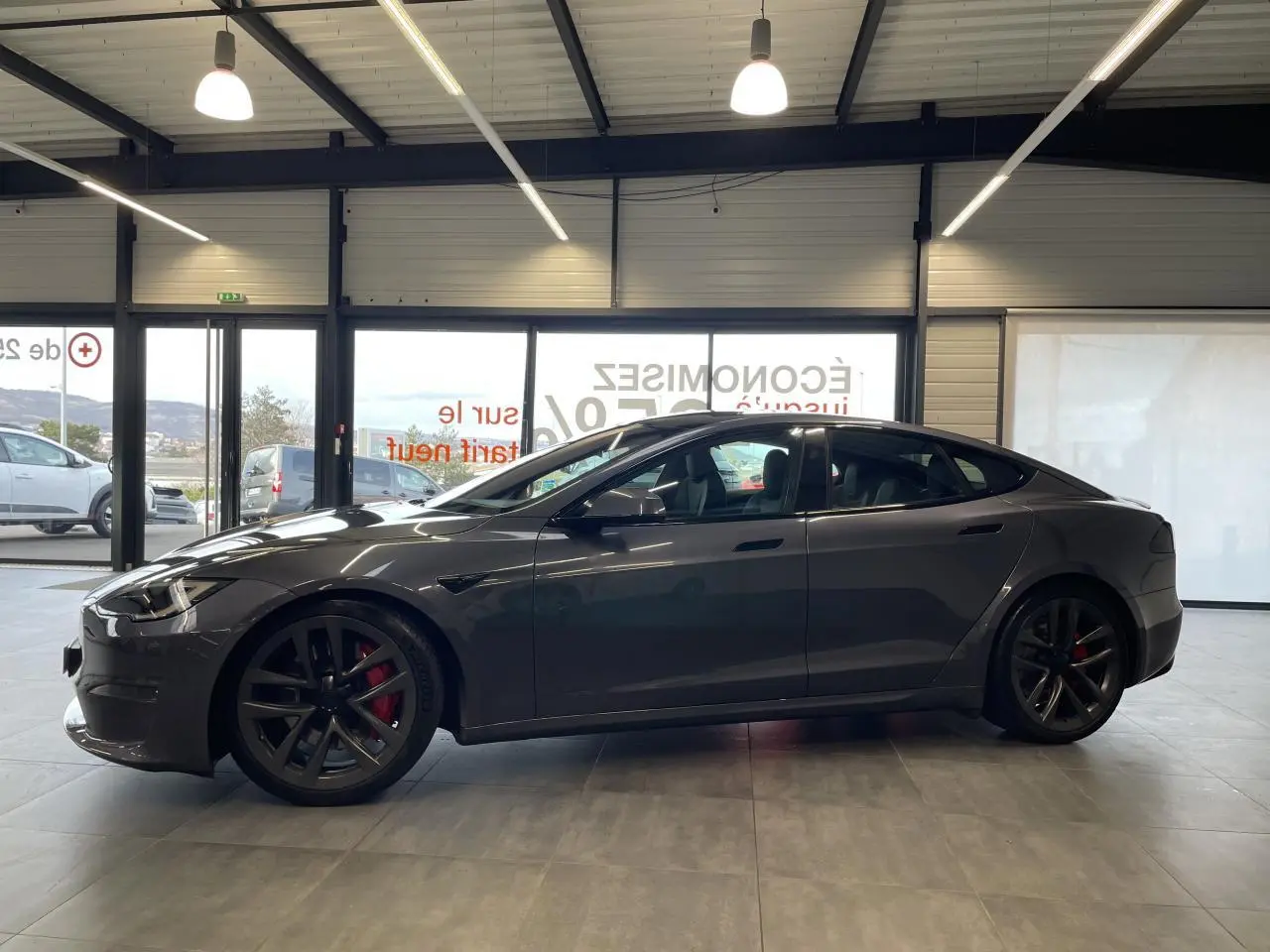 Tesla Model S Plaid gris foncé vue de profil côté gauche, jantes noires avec étriers de frein rouges, intérieur visible.