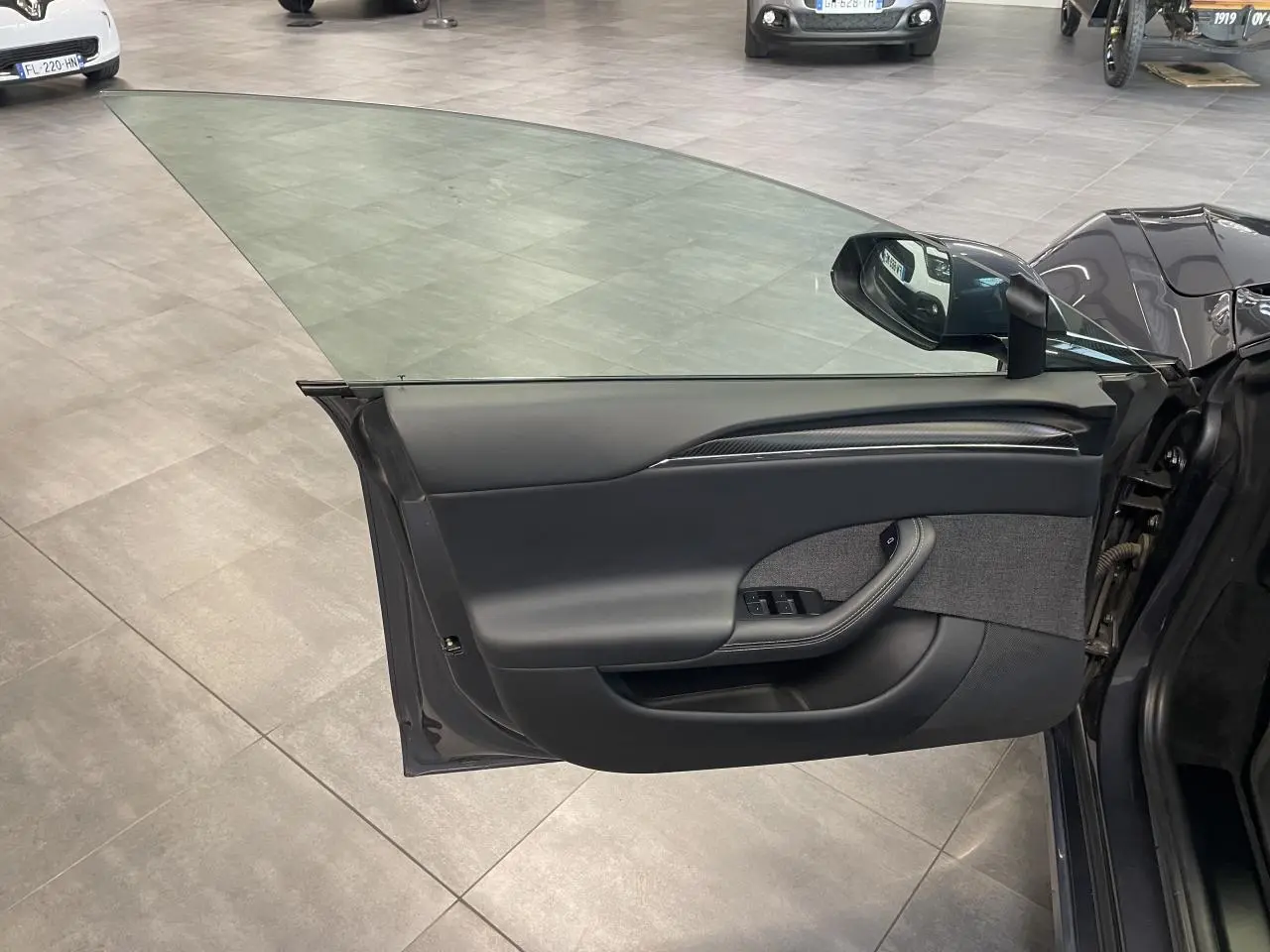 Vue de la porte avant gauche ouverte d'une Tesla Model S Plaid 2023 gris foncé, intérieur noir avec inserts carbone.