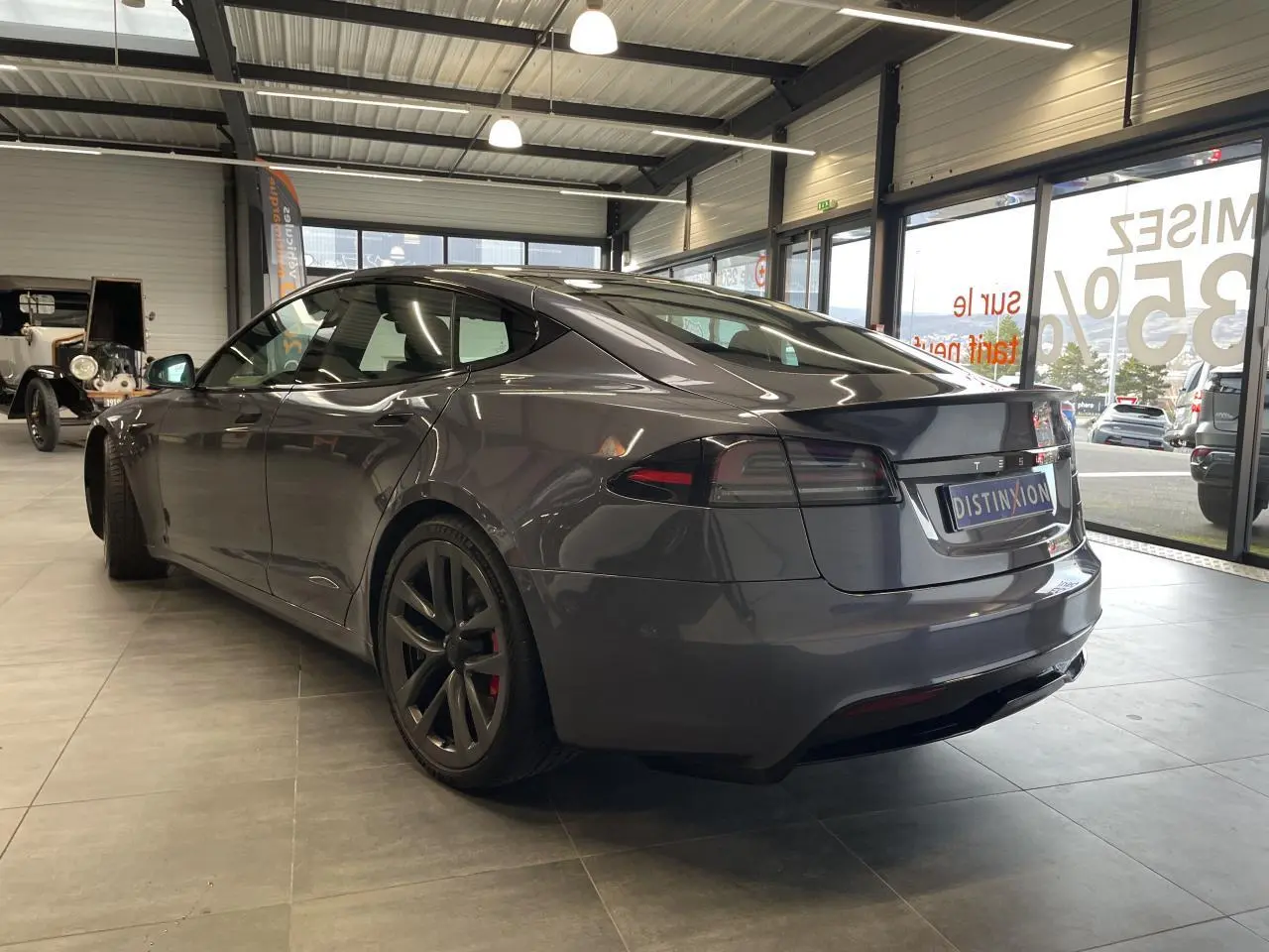 Tesla Model S Plaid gris foncé vue 3/4 arrière droit en intérieur avec jantes noires et spoiler arrière.