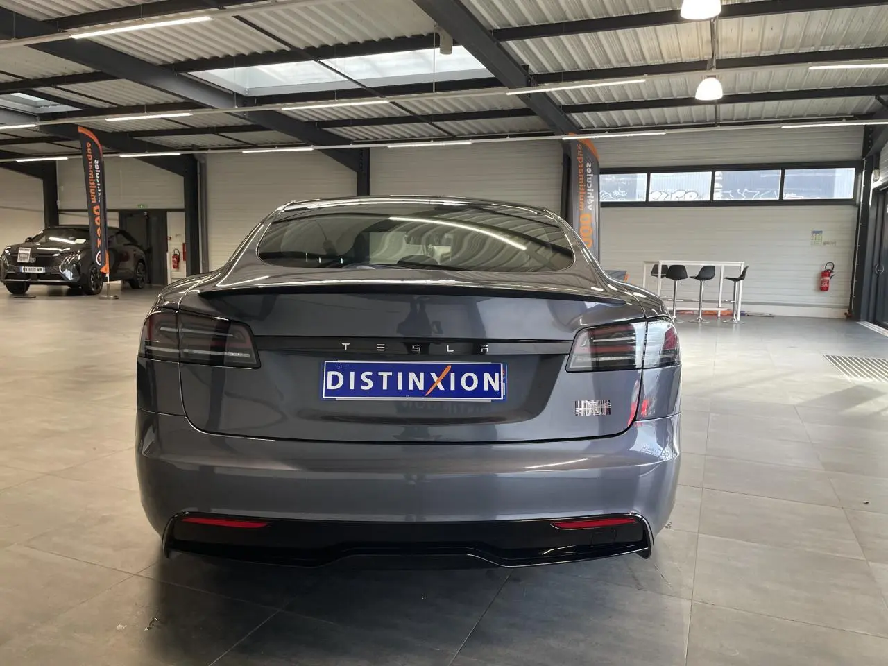 Vue arrière d'une Tesla Model S Plaid gris foncé dans un showroom avec feux arrière LED fumés.