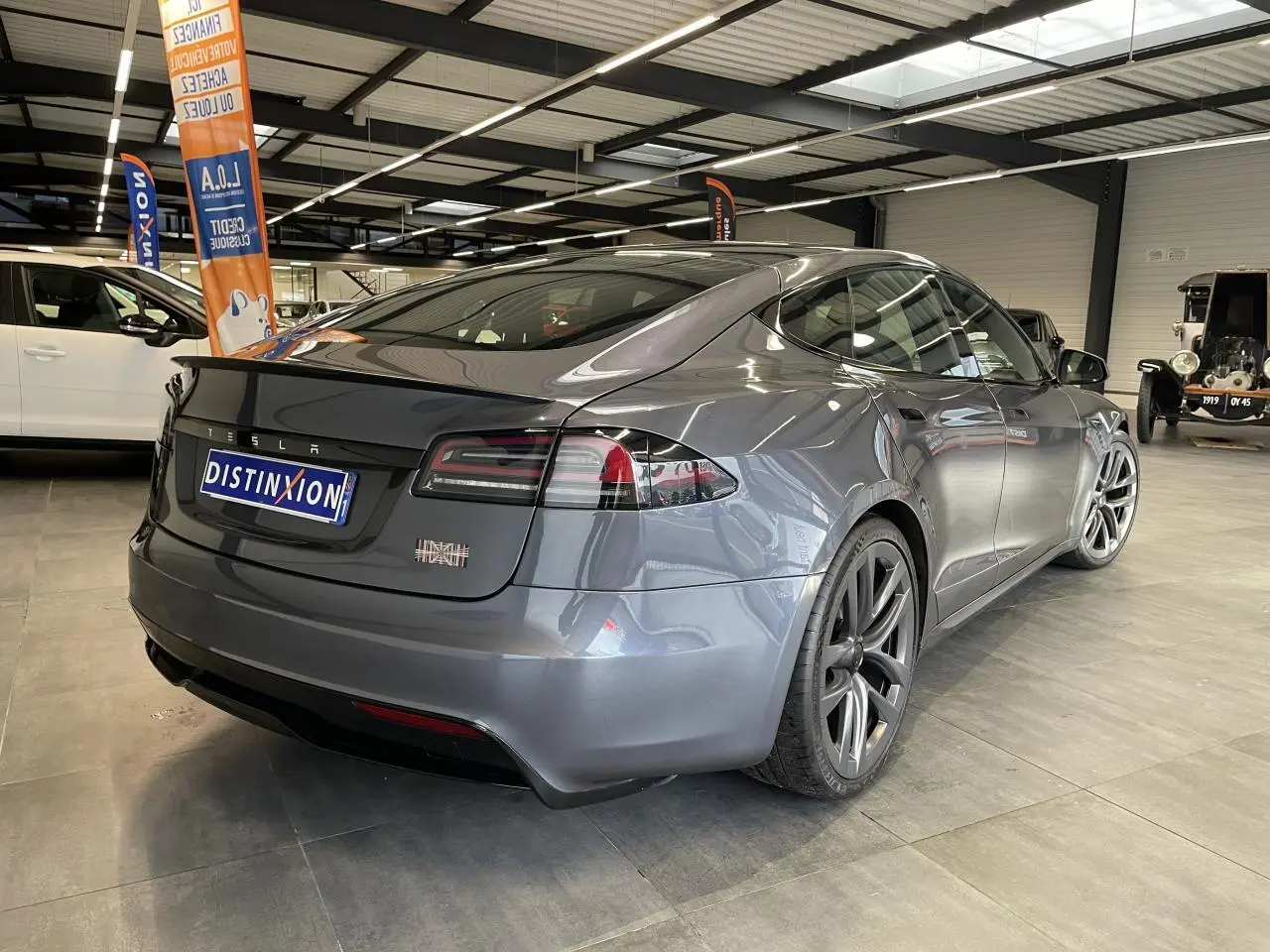 Tesla Model S Plaid gris foncé vue 3/4 arrière droit en intérieur avec jantes aluminium distinctives.