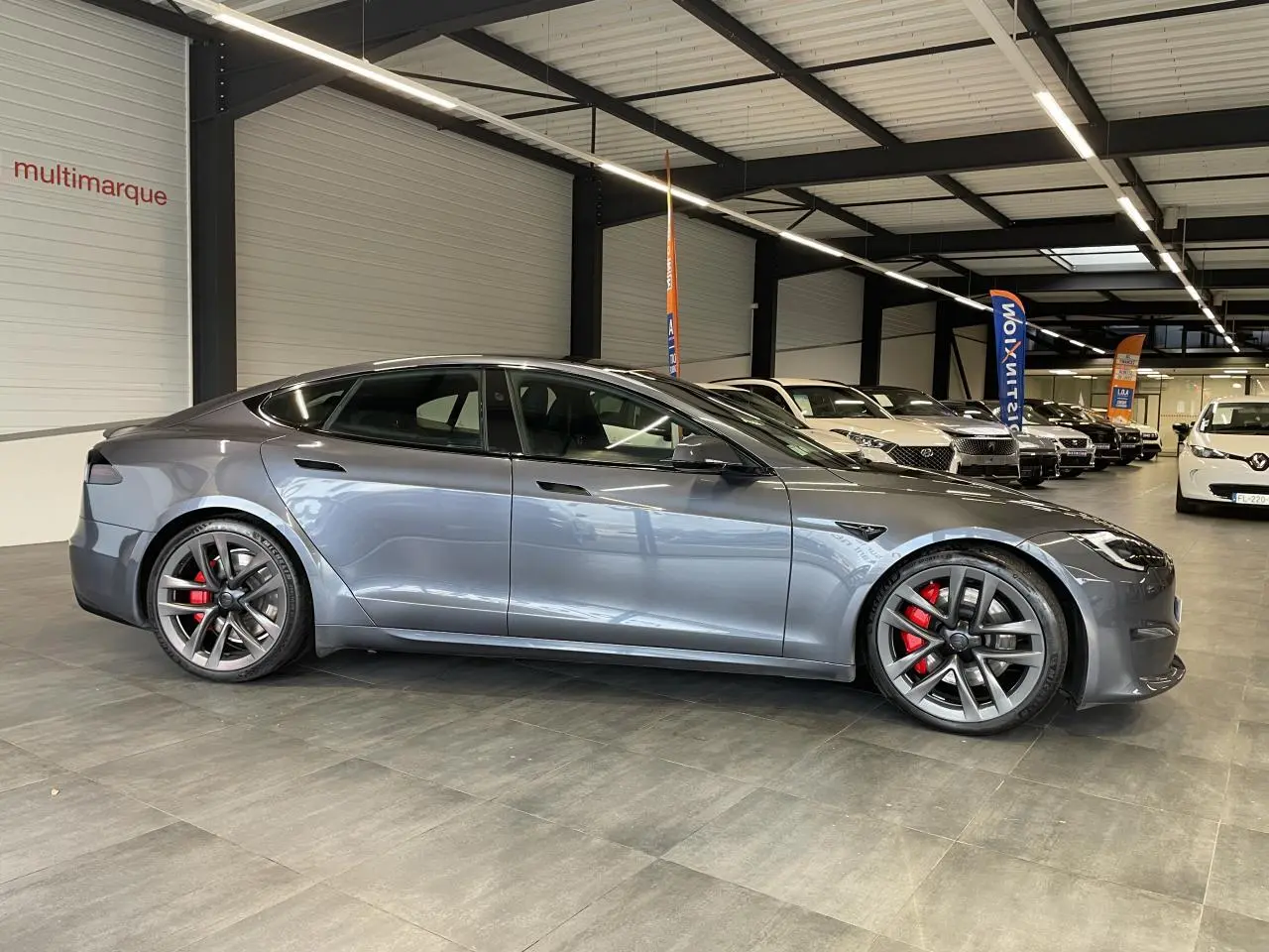 Tesla Model S Plaid gris foncé vue de profil côté gauche dans un showroom avec jantes sport et étriers rouges.