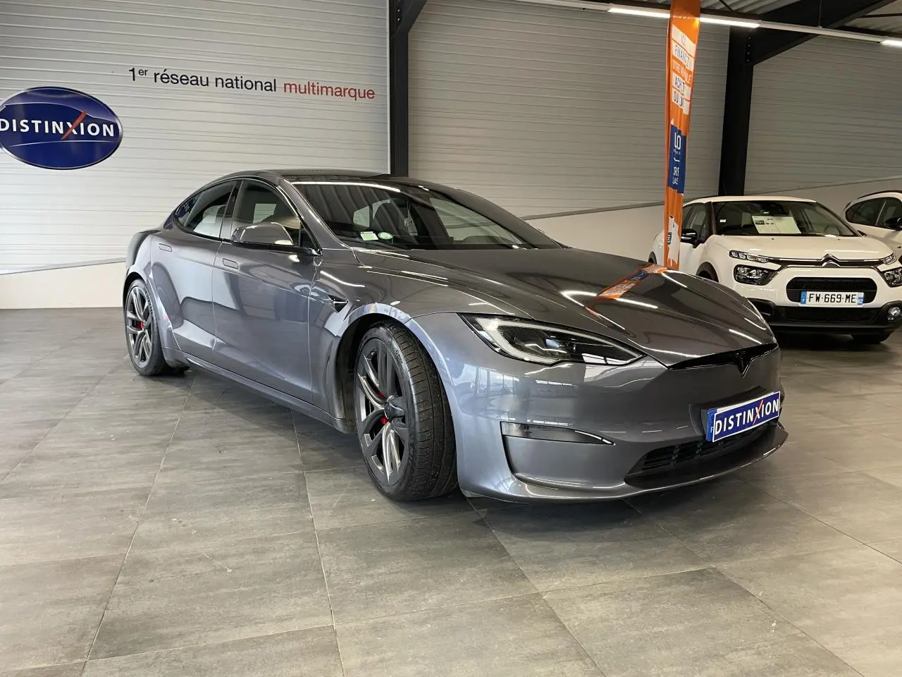 Tesla Model S Plaid gris foncé vue 3/4 avant en intérieur avec jantes sport et calandre lisse.