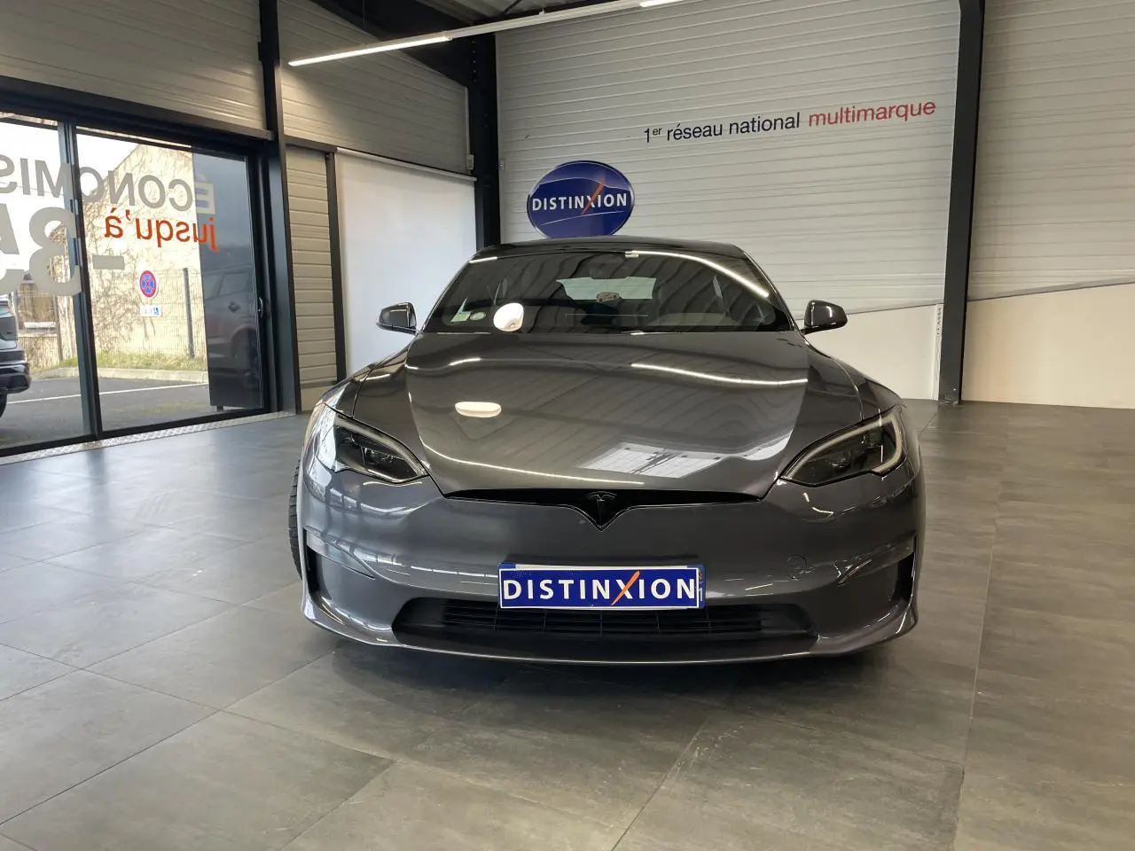 Tesla Model S Plaid gris foncé vue de face dans un showroom avec reflets sur la carrosserie lisse.