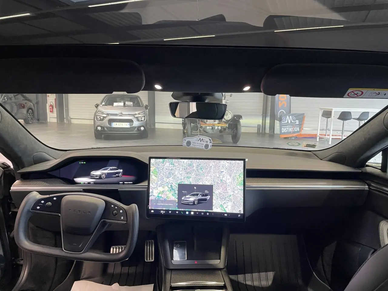 Vue intérieure avant du Tesla Model S Plaid 2023 gris foncé, avec grand écran tactile central et volant yoke.
