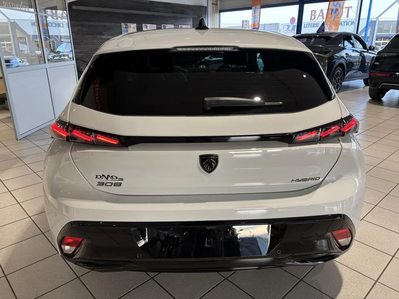 Vue arrière d'une Peugeot 308 Hybrid blanche Okenite avec feux arrière LED en forme de griffes et logo lion central.