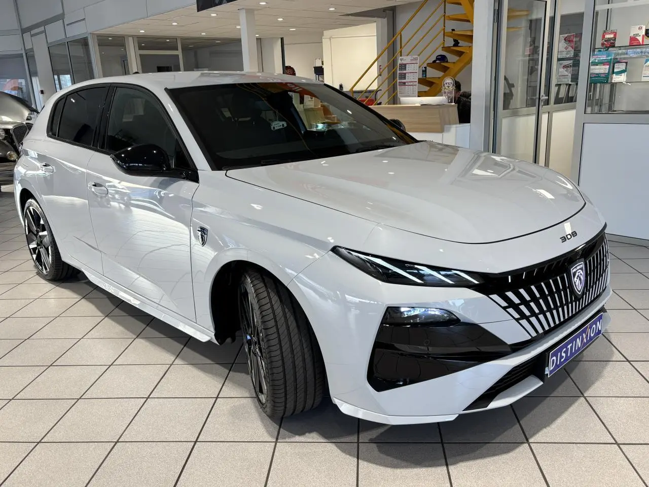 Peugeot 308 blanc Okenite vue 3/4 avant droit, calandre noire distinctive et jantes alliage bi-ton.