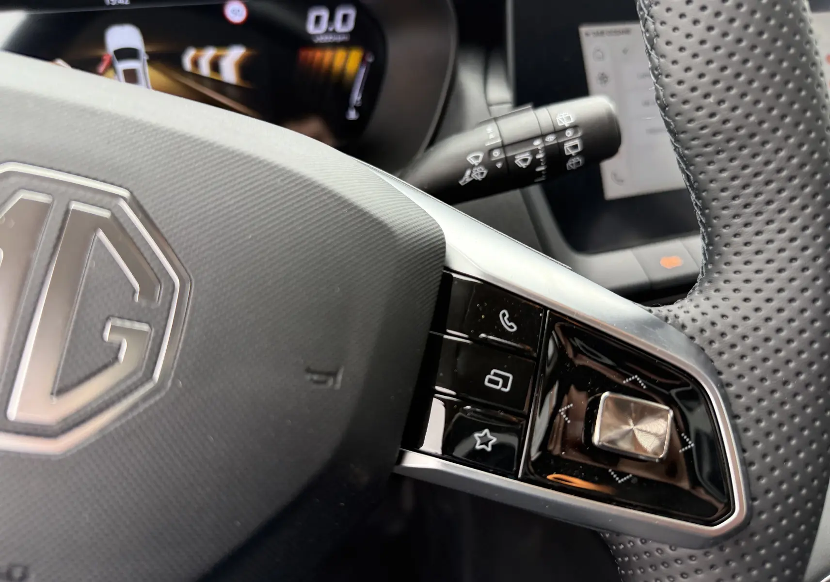 Gros plan sur le volant perforé du MG ZS 1.5L Hybrid+ 197ch, avec commandes intégrées et logo MG visible.