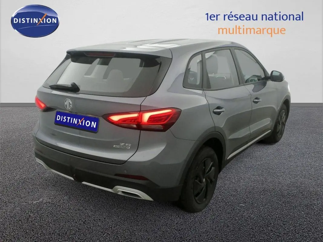 Vue 3/4 arrière droite du SUV MG ZS hybride gris Hampstead avec feux arrière allumés sur fond neutre.