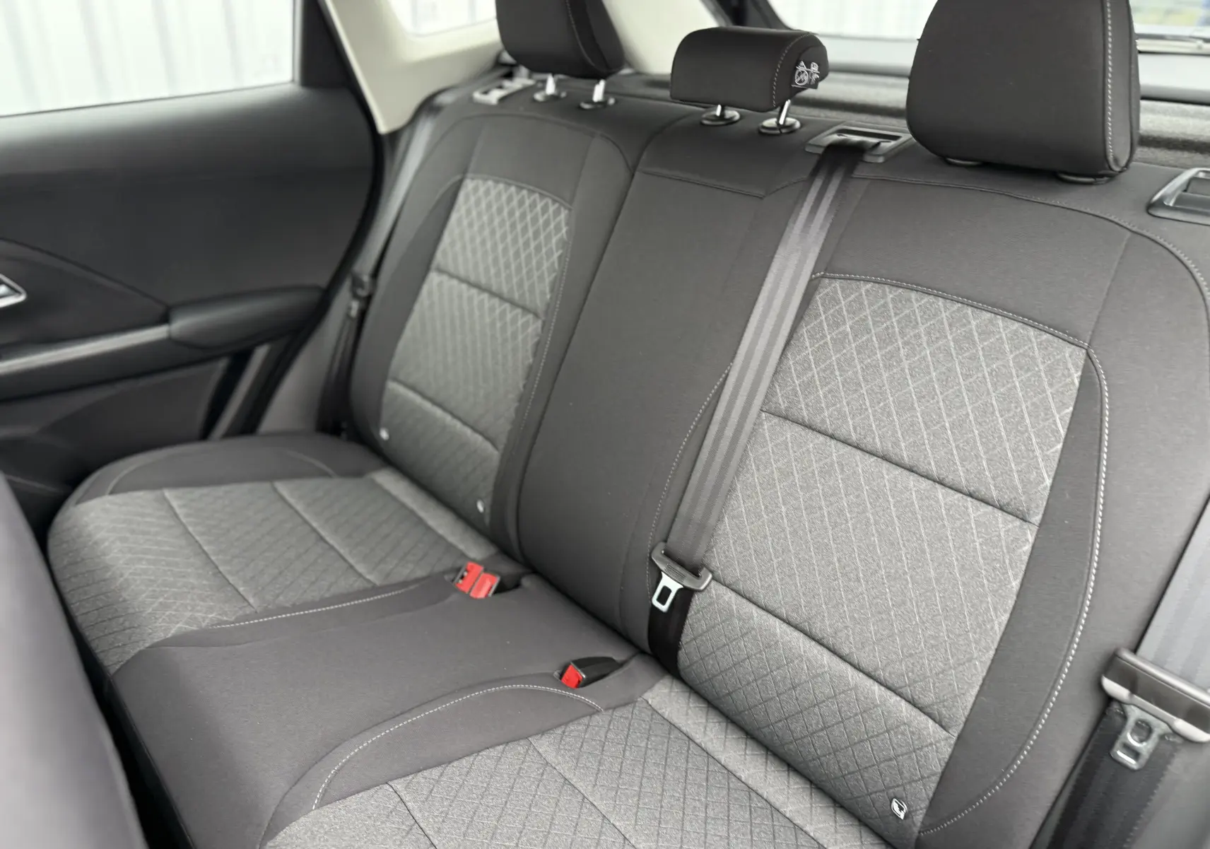 Vue intérieure du siège arrière droit de la MG ZS 1.5L Hybrid+ 2026 avec tissu gris à motifs losanges et ceinture noire.
