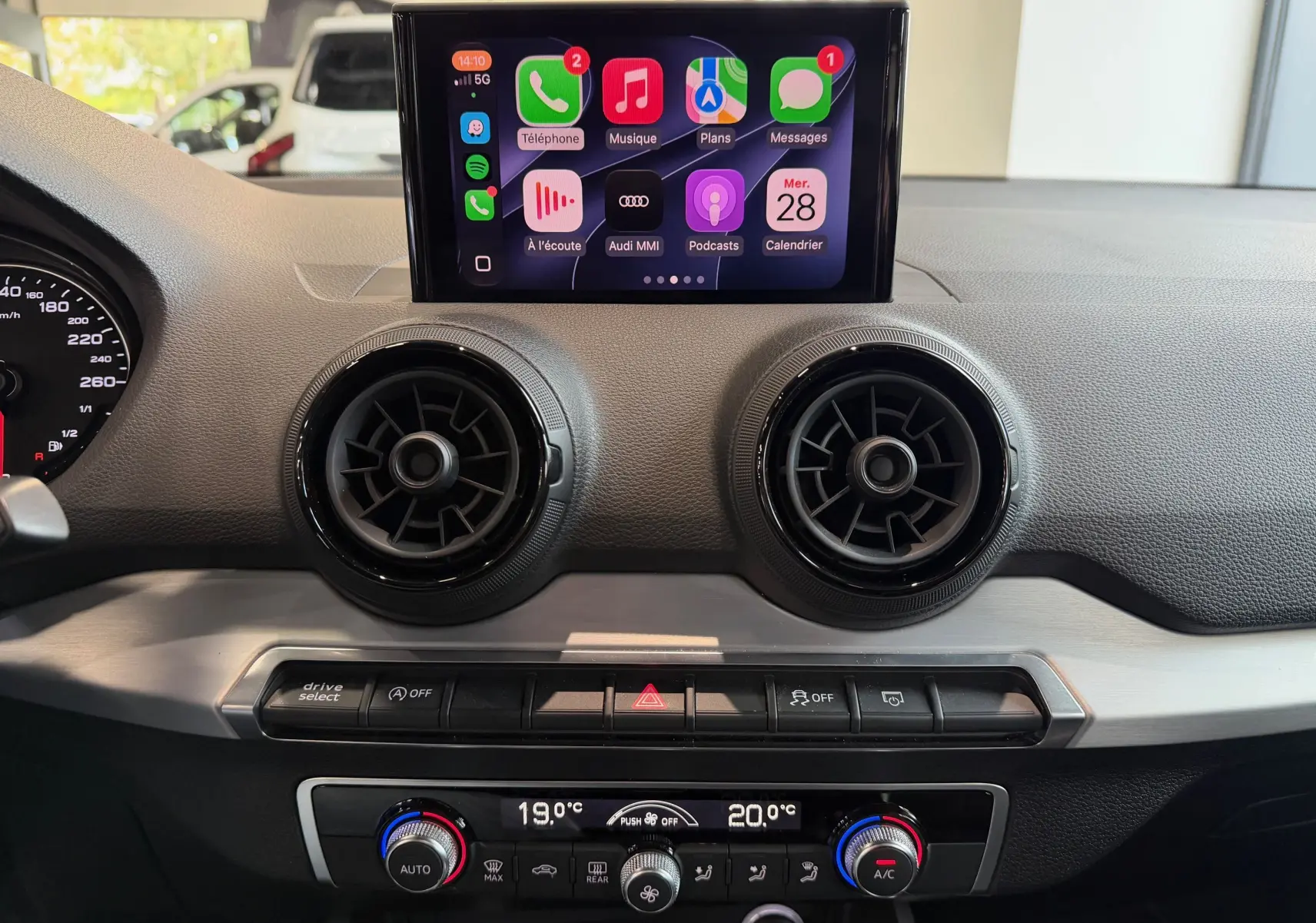 Vue intérieure du tableau de bord de l'Audi Q2 gris, avec écran tactile central affichant Apple CarPlay et aérateurs ronds noirs.