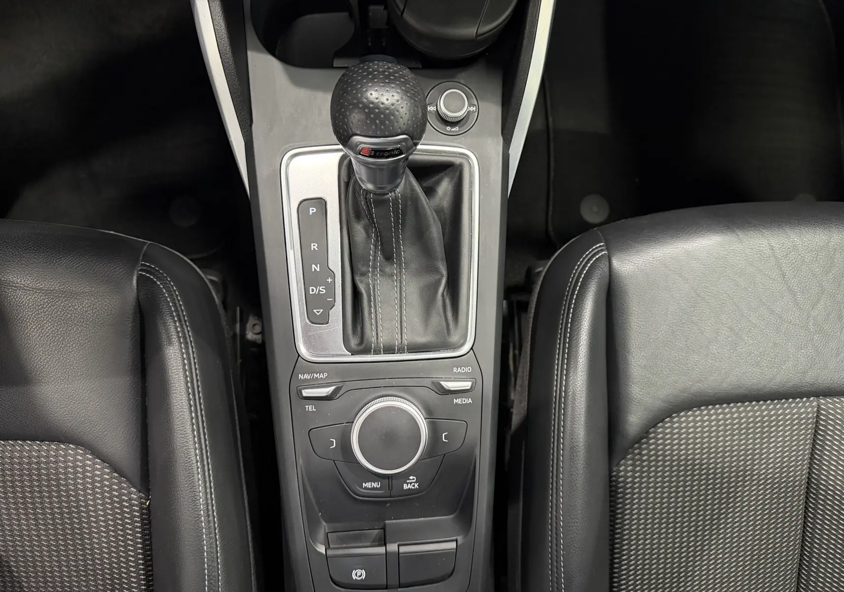 Vue plongeante sur la console centrale noire de l'Audi Q2 2.0 TDI 190 S-Line avec levier de vitesses automatique et sièges en cuir partiel.