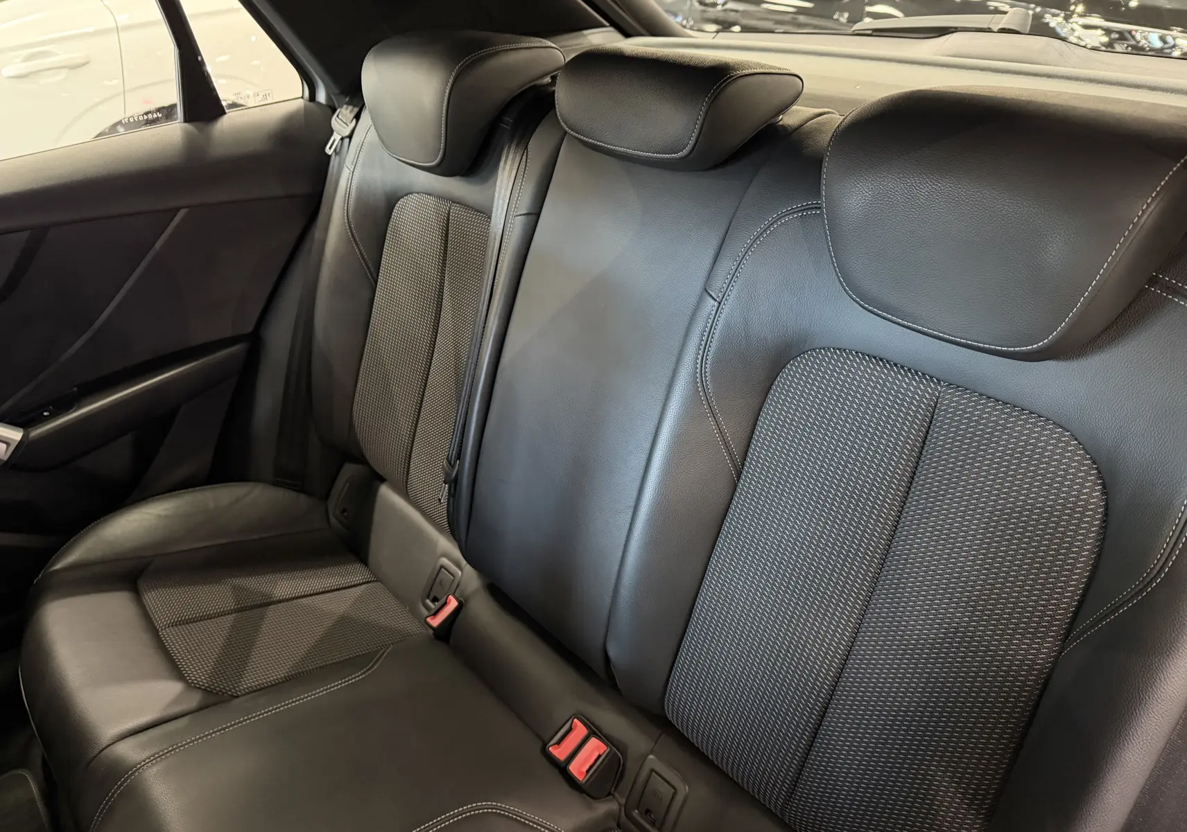 Vue intérieure des sièges arrière en cuir noir de l'Audi Q2, mettant en valeur les appuie-têtes et les ceintures de sécurité.
