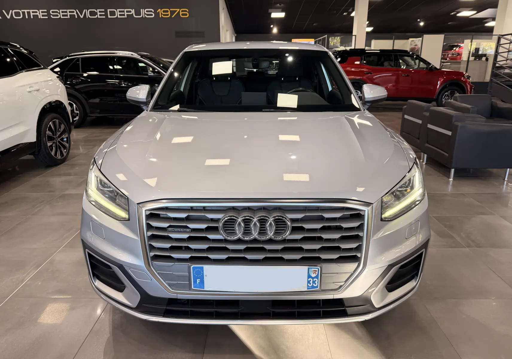 Audi Q2 gris vue de face en intérieur, avec calandre hexagonale et feux LED allumés.