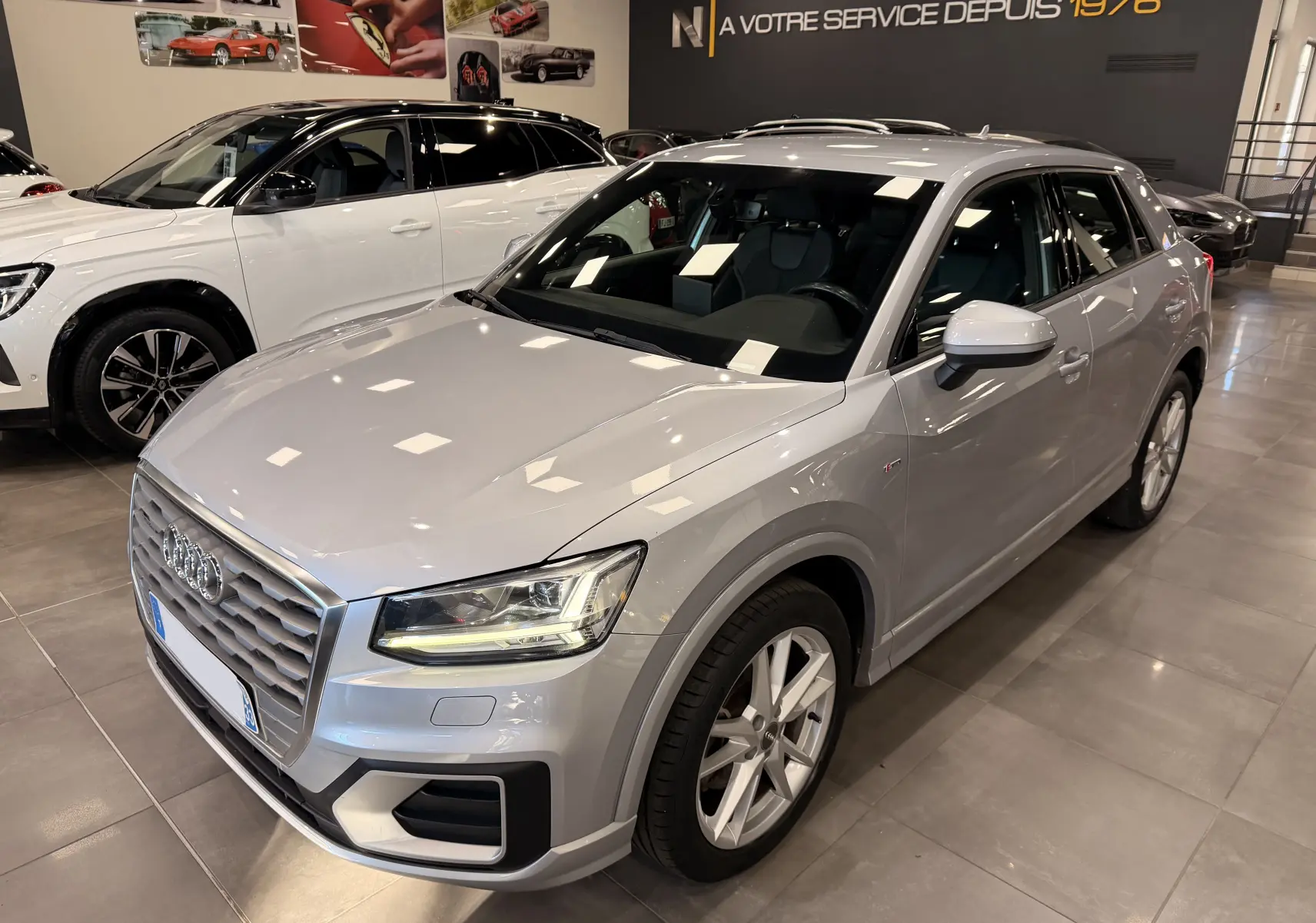 Audi Q2 gris vue 3/4 avant droit en intérieur, mettant en valeur sa calandre et ses phares LED distinctifs.
