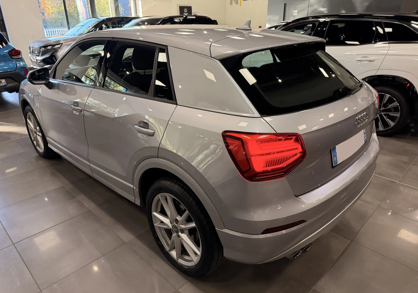 Audi Q2 gris vue 3/4 arrière droit en intérieur, avec feux arrière LED et jantes alliage 18 pouces S-Line.
