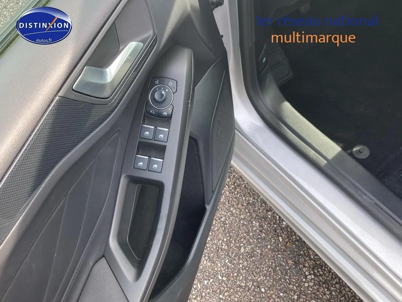 Gros plan sur la portière côté conducteur gris avec commandes électriques et haut-parleur intégré.