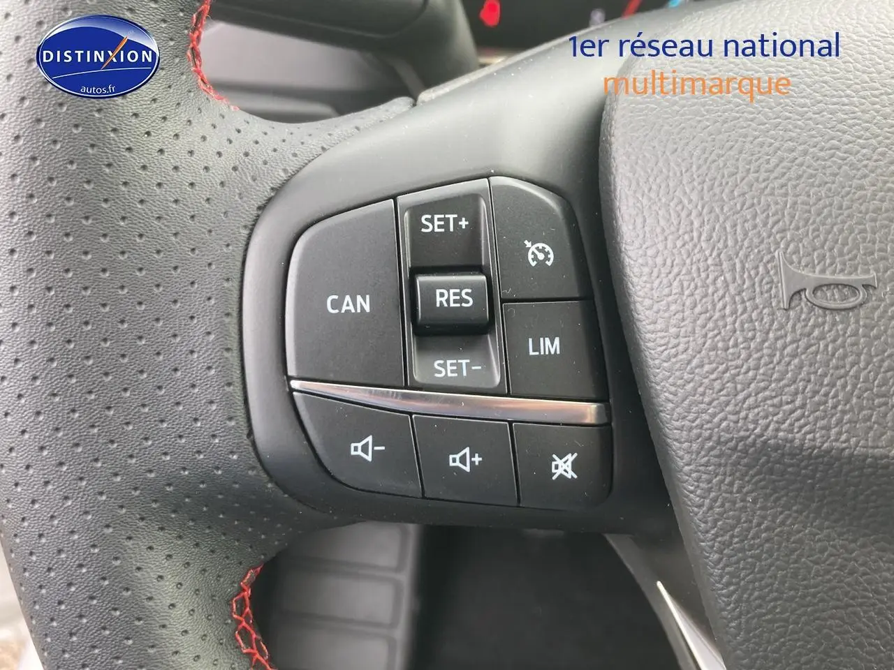 Gros plan sur le volant perforé noir avec coutures rouges et commandes de régulateur de vitesse de la Ford Focus gris 2025.