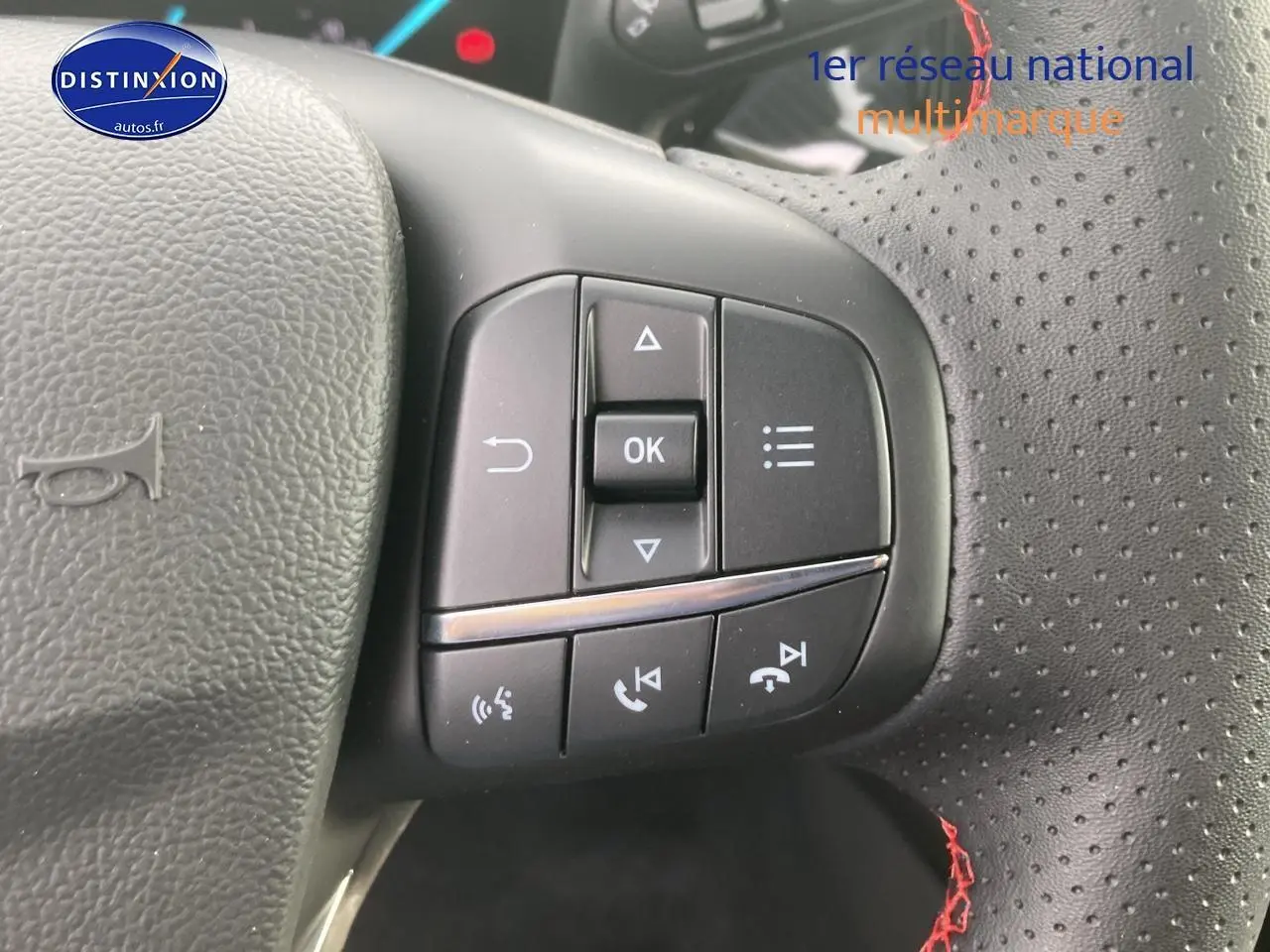 Vue rapprochée des commandes multifonctions côté gauche du volant perforé avec coutures rouges d'une Ford Focus gris 2025.