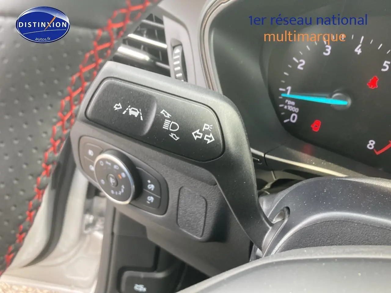 Gros plan sur la commande de clignotants et volant avec surpiqûres rouges d'une Ford Focus gris 2025.