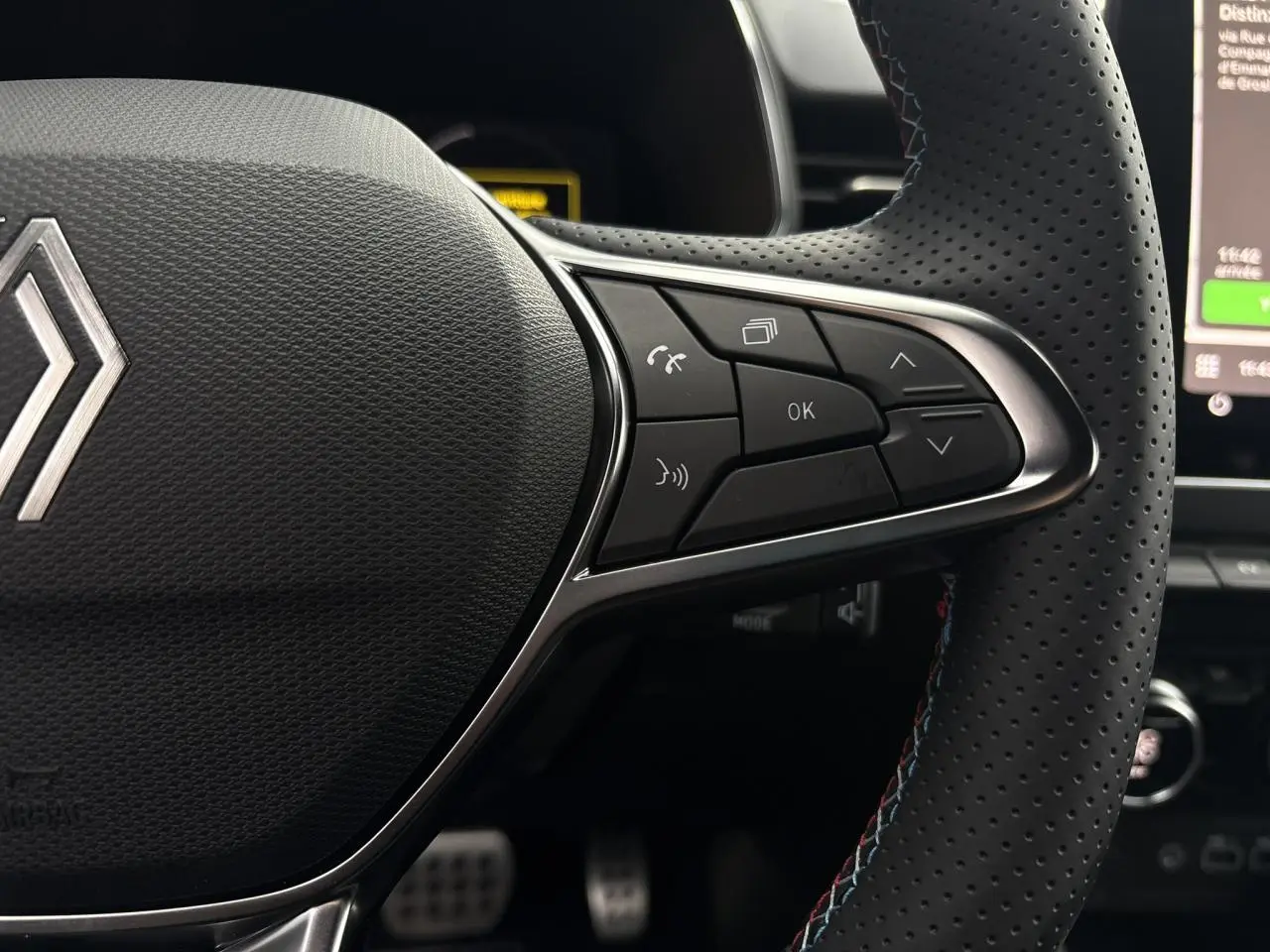 Gros plan sur le côté droit du volant perforé de la Renault Clio 2025 avec commandes multifonctions et surpiqûres bleues.