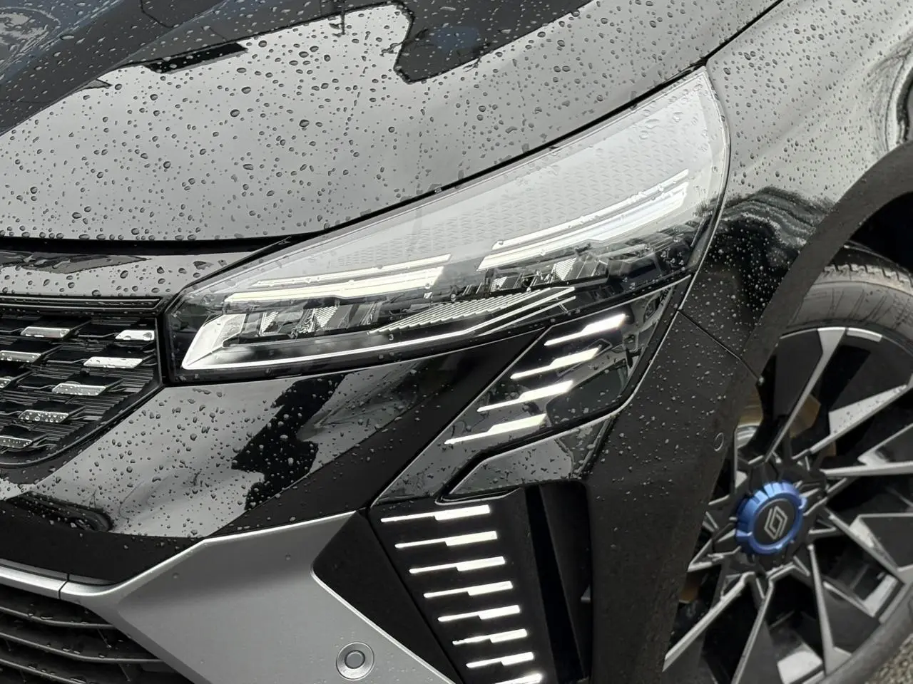 Gros plan sur l'avant droit noir étoilé de la Renault Clio 2025 avec phares LED et jante alliage distinctive.