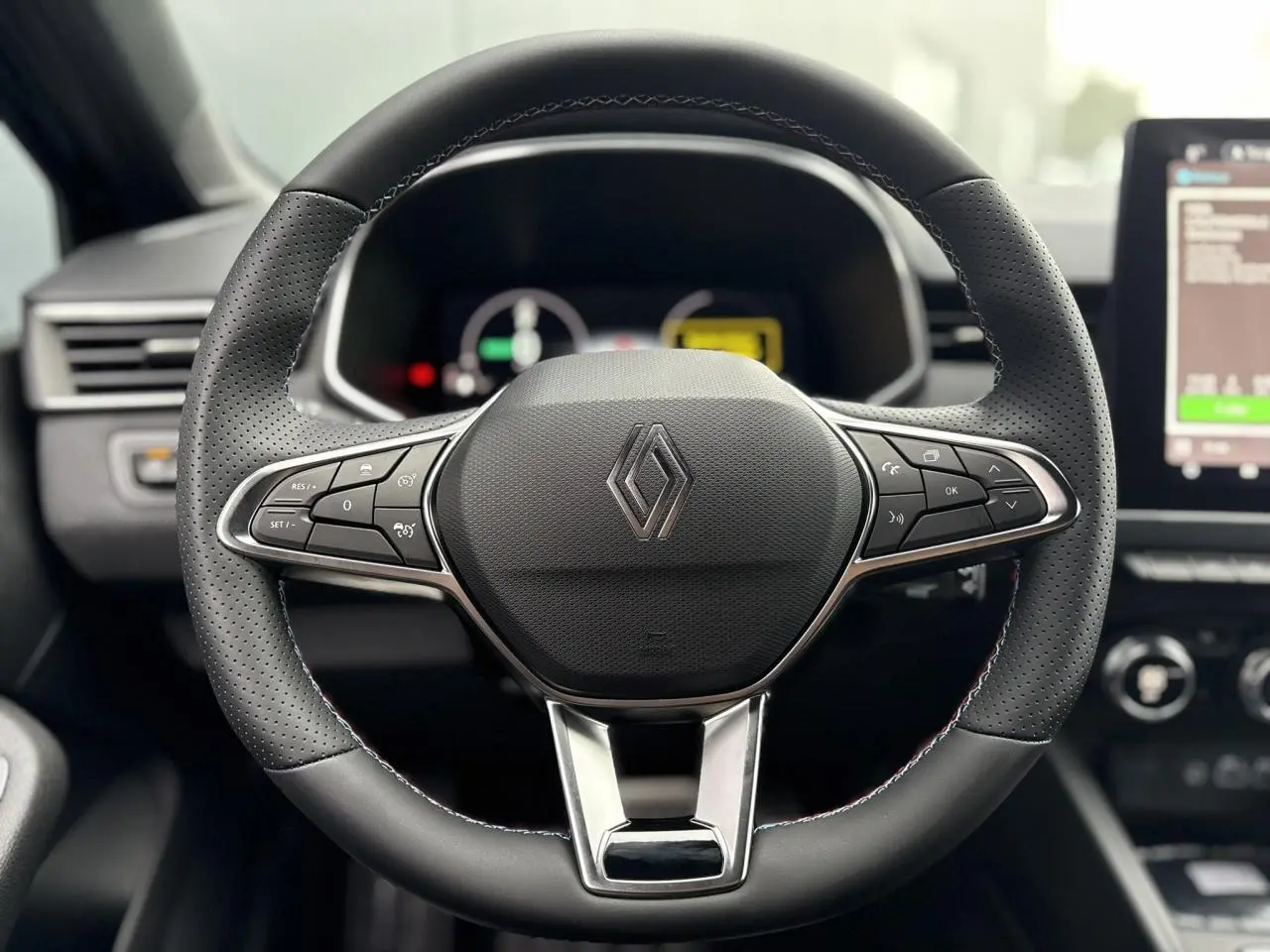 Volant multifonction en cuir noir avec logo Renault, tableau de bord numérique et écran tactile à droite.